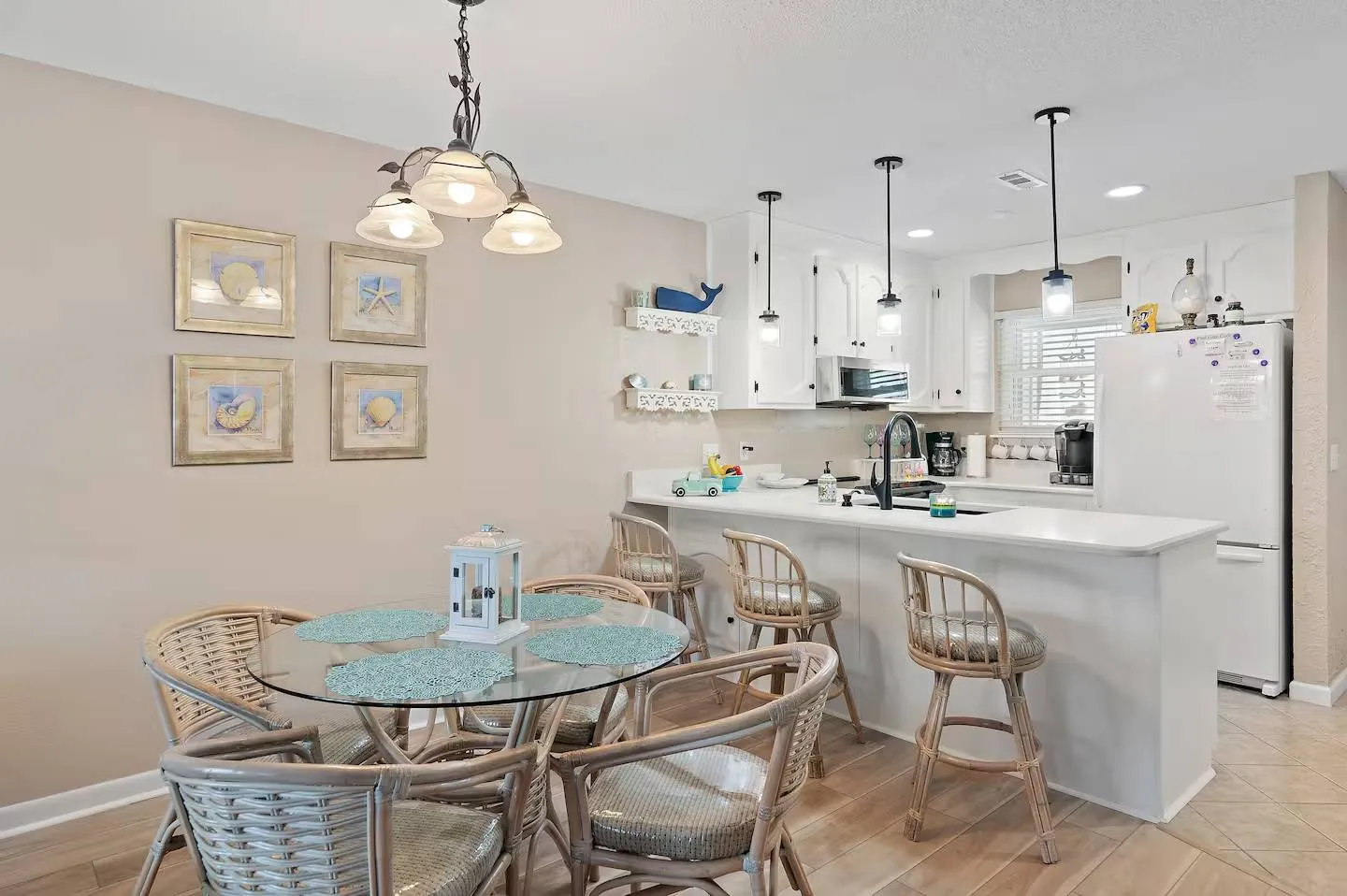 Dining area with a round glass table and wicker chairs next to an open kitchen with a breakfast bar and white cabinetry.