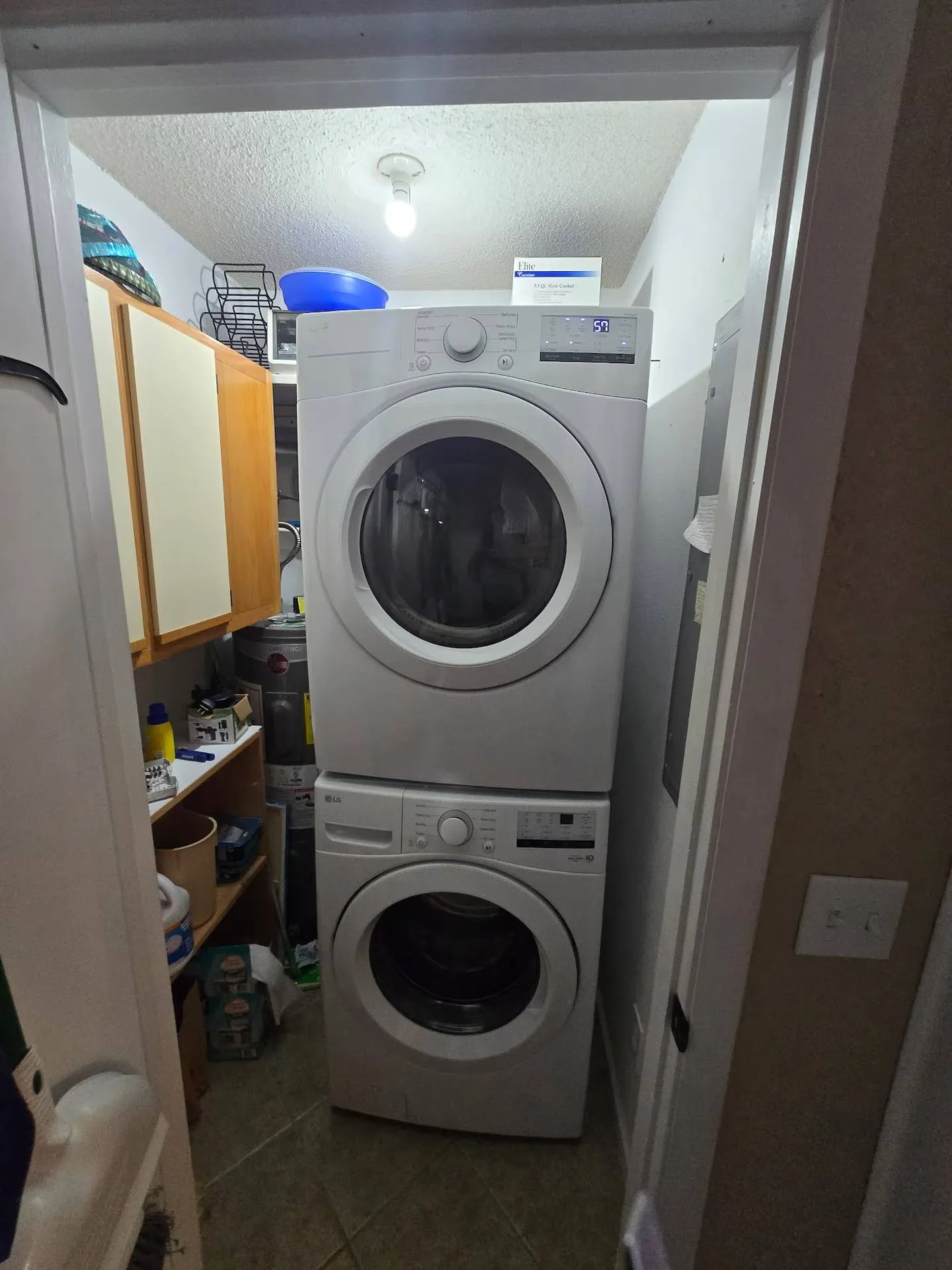 A stacked front-loading washer and dryer in a compact utility closet with storage shelves and a water heater.