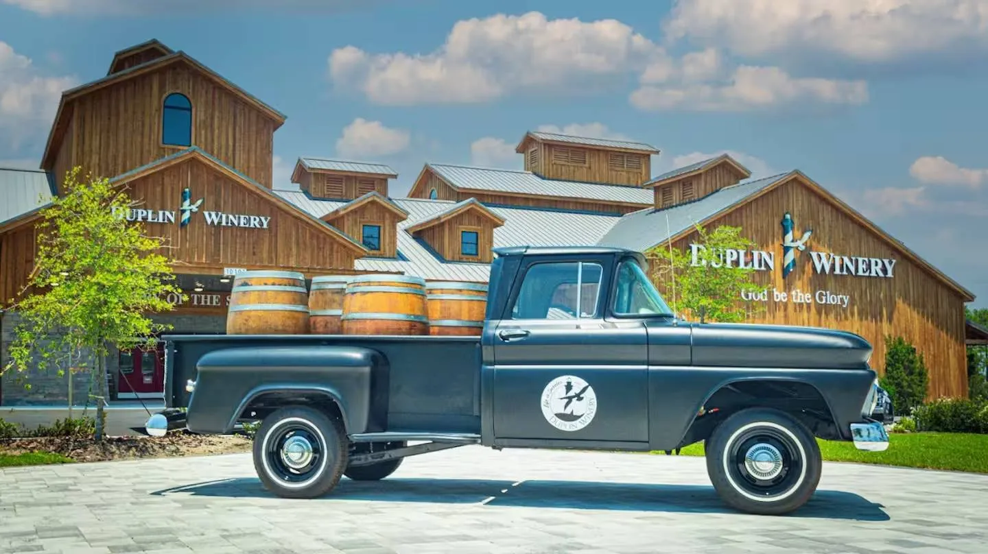 Vintage black pickup truck loaded with wooden barrels parked in front of Duplin Winery.