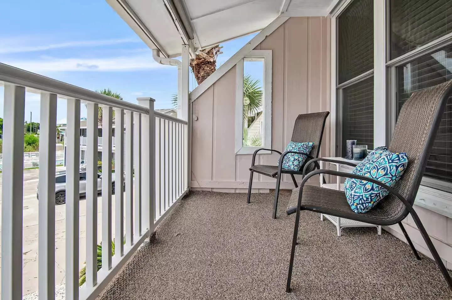Covered outdoor balcony with white railings, textured flooring, and two armchairs with patterned pillows.