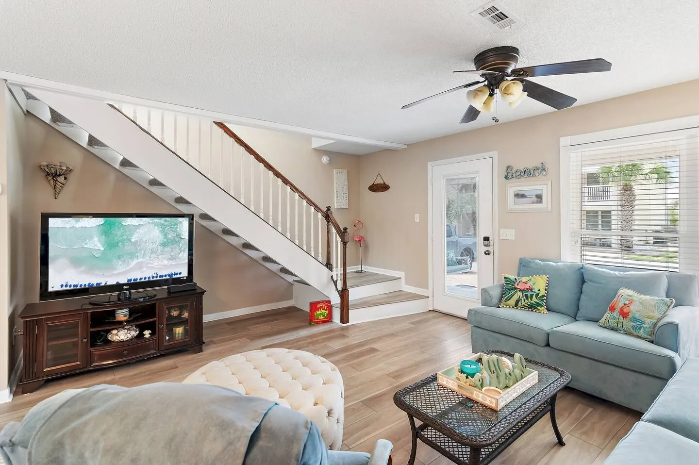 Living room featuring wood-look floors, a blue sofa, a TV on a wooden console, and a staircase leading upstairs.