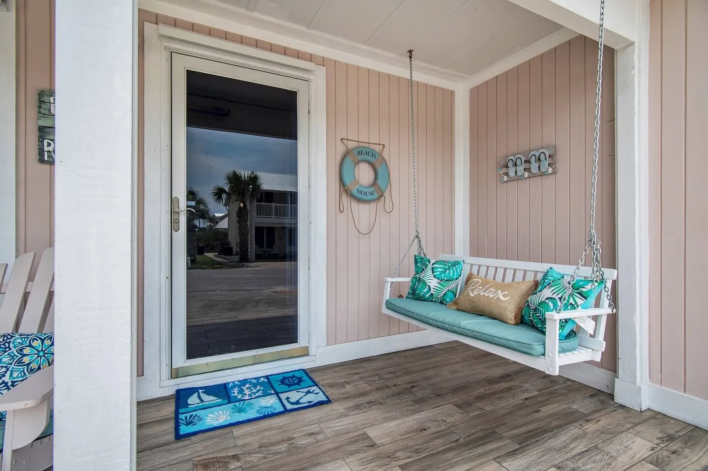 Porch entryway with a white suspended porch swing, light pink siding, wood-look plank flooring, and a glass storm door.