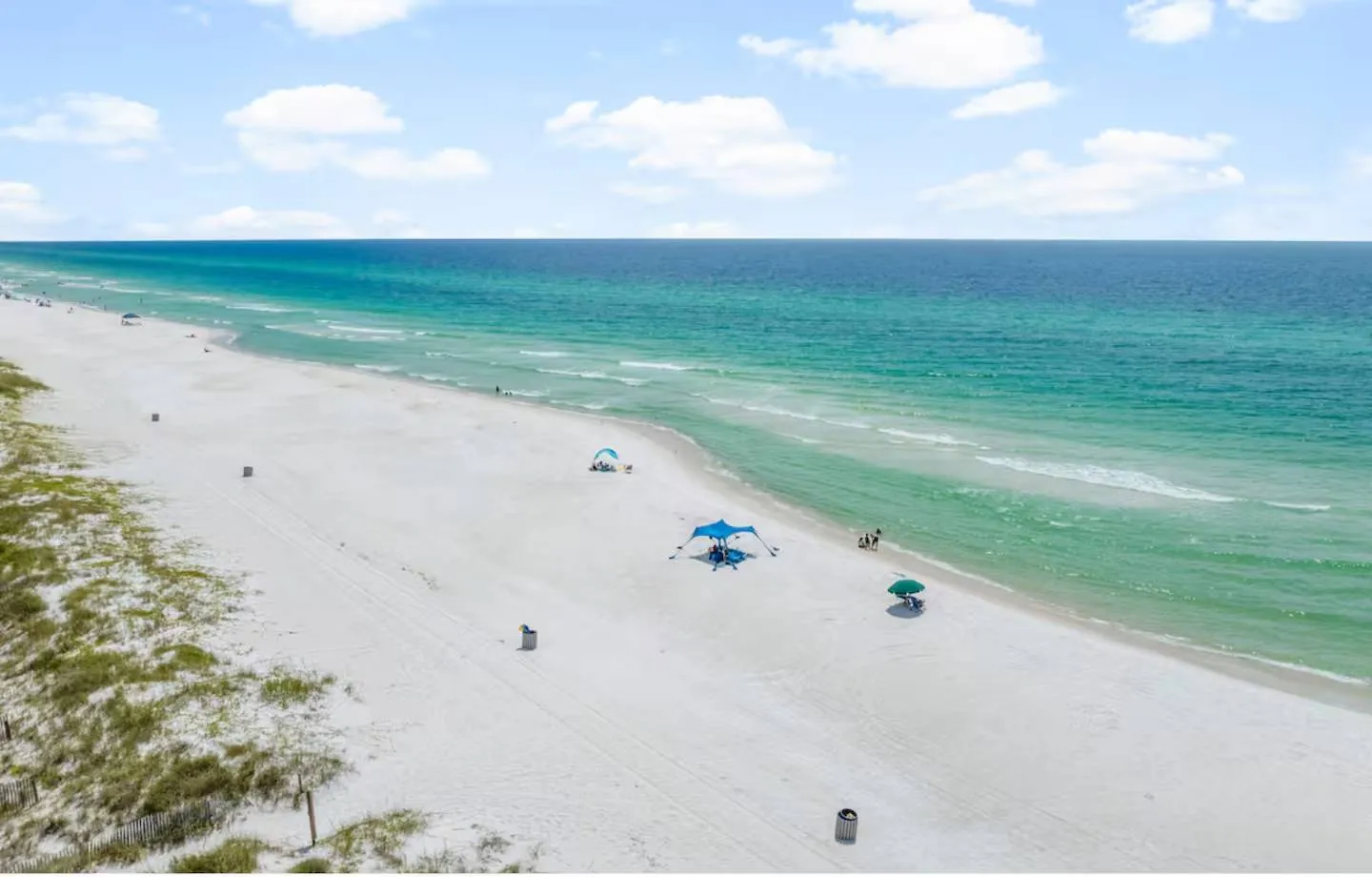 Aerial view of a wide white-sand beach and turquoise ocean water under a partly cloudy sky.