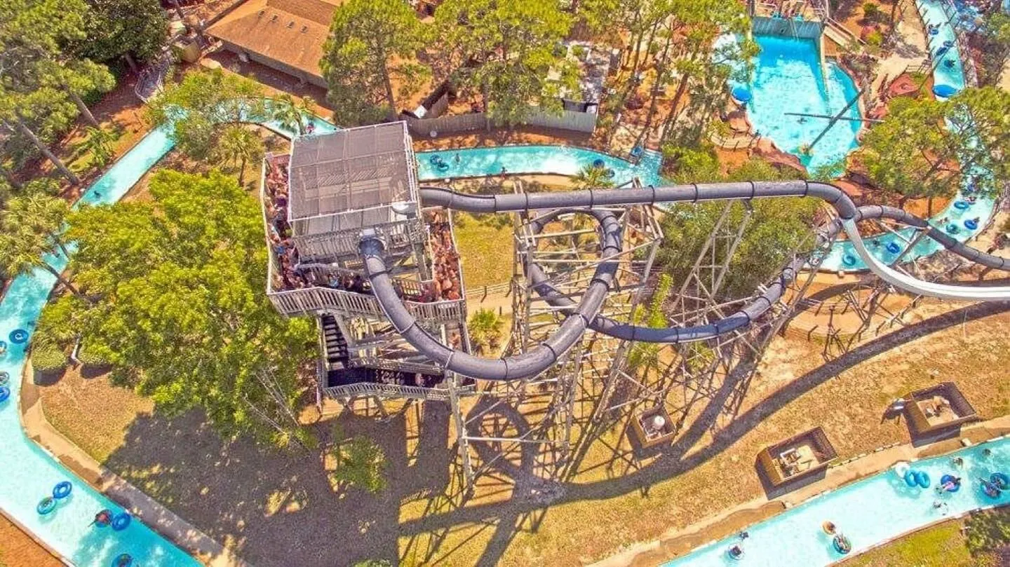 Aerial view of a water park featuring a tall slide tower with an enclosed tube slide winding over a lazy river.