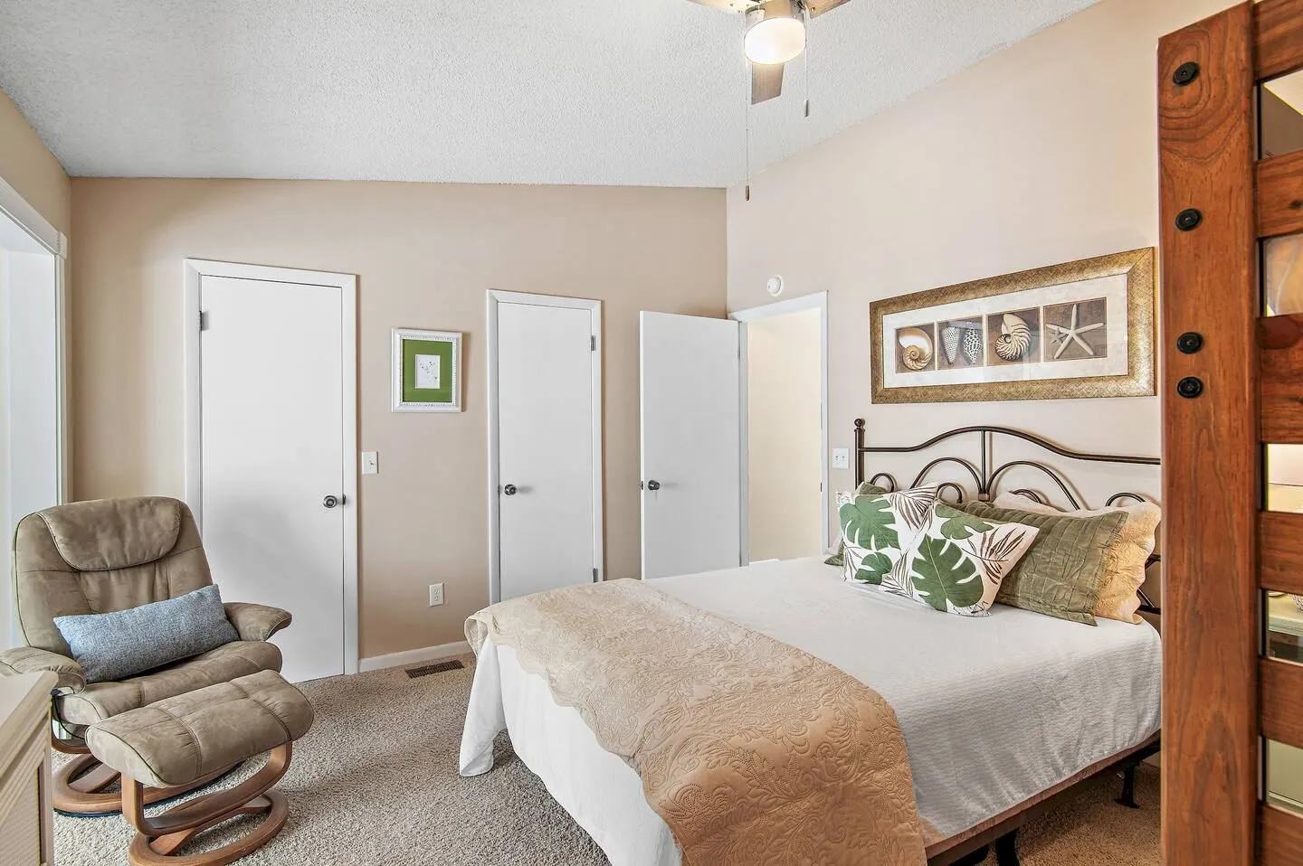 Bedroom featuring a made bed with an iron headboard, an upholstered armchair with an ottoman, and light carpeting.