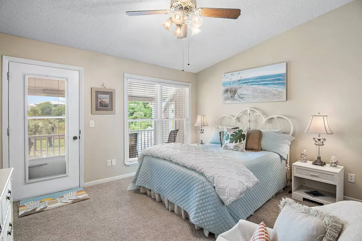 Bedroom with carpeted floor, light blue bedding on a wrought iron bed, ceiling fan, and glass door leading to an outdoor balcony.