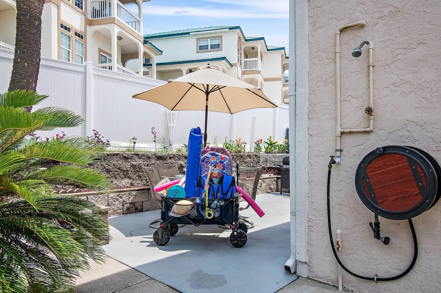 Outdoor patio area featuring a beach wagon packed with gear under an umbrella next to an outdoor shower fixture mounted on the wall.