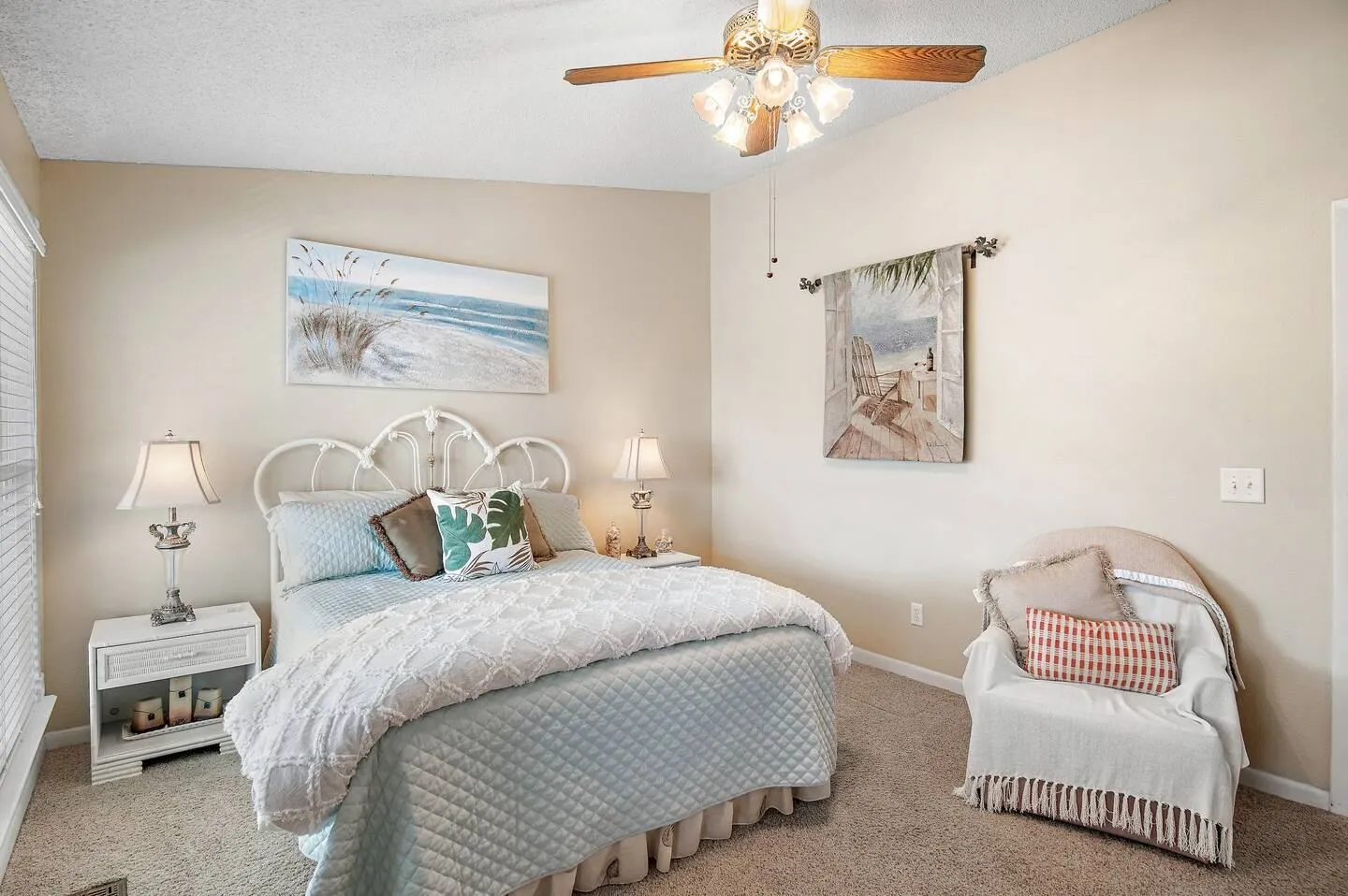 Bedroom with a white metal headboard, light blue bedspread, matching nightstands with lamps, and an armchair.