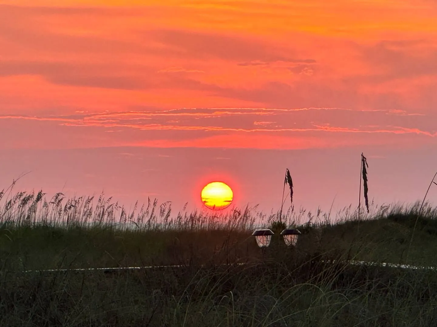 Bright sunset glowing over dunes and sea oats with two small pathway lights.