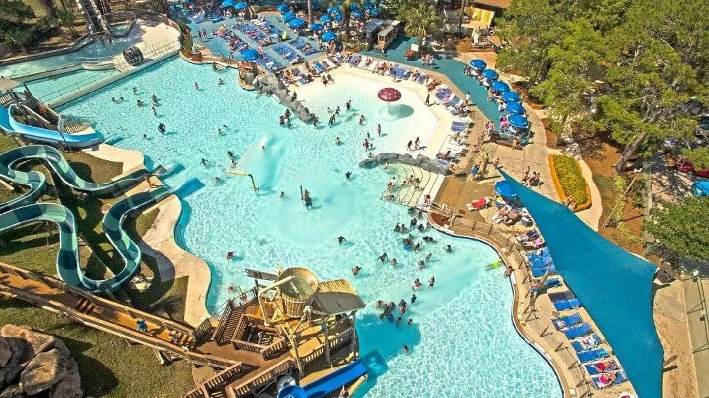 Aerial view of a large resort-style pool with water slides, play structures, and surrounding lounge chairs.
