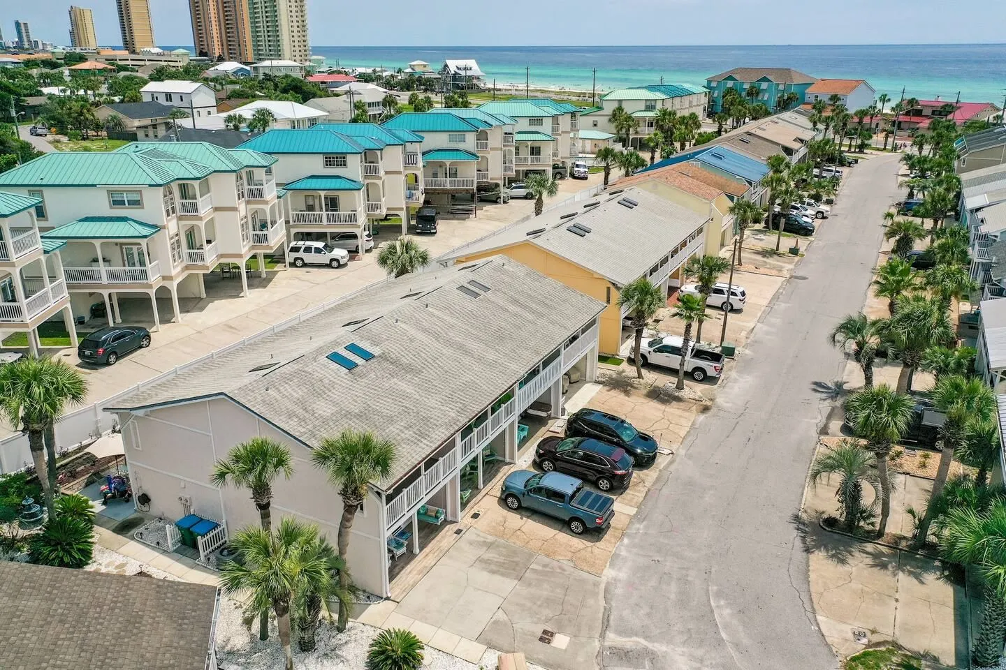 Aerial view of a coastal residential street lined with multi-level homes and townhouses near the beach.