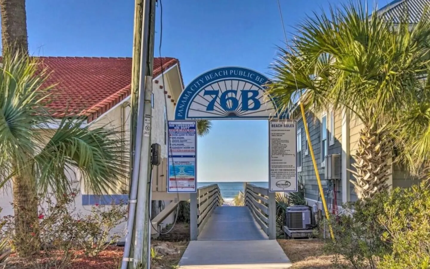 Public beach access ramp 76B leading between buildings directly toward the ocean and sand under a blue sky.