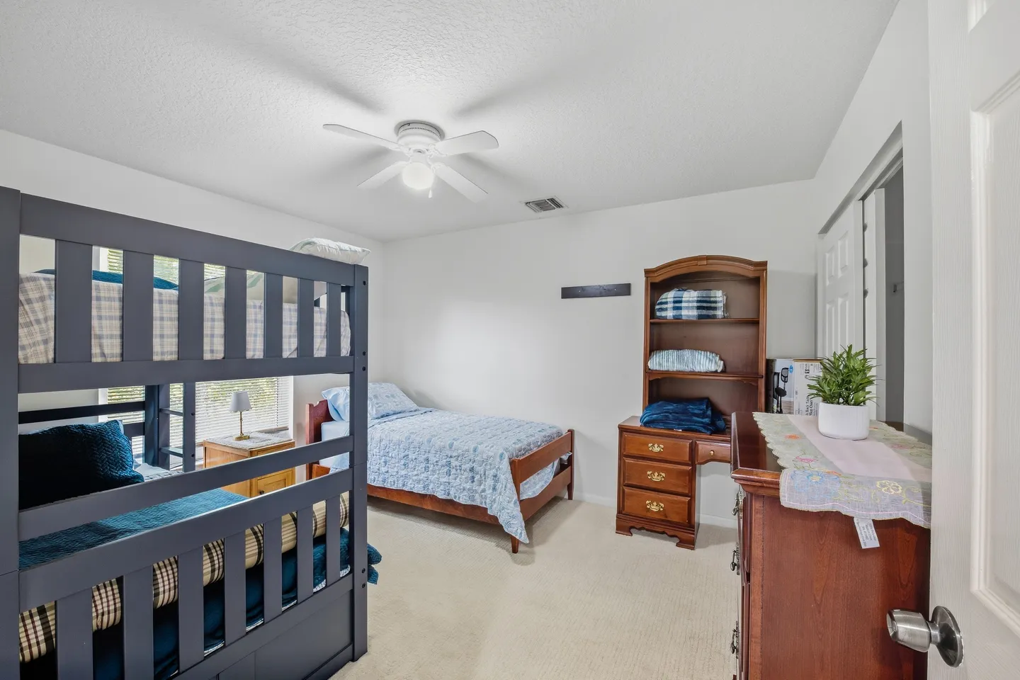 Bedroom featuring a dark-painted bunk bed, a single bed with a light blue quilt, wooden dressers, and a ceiling fan.