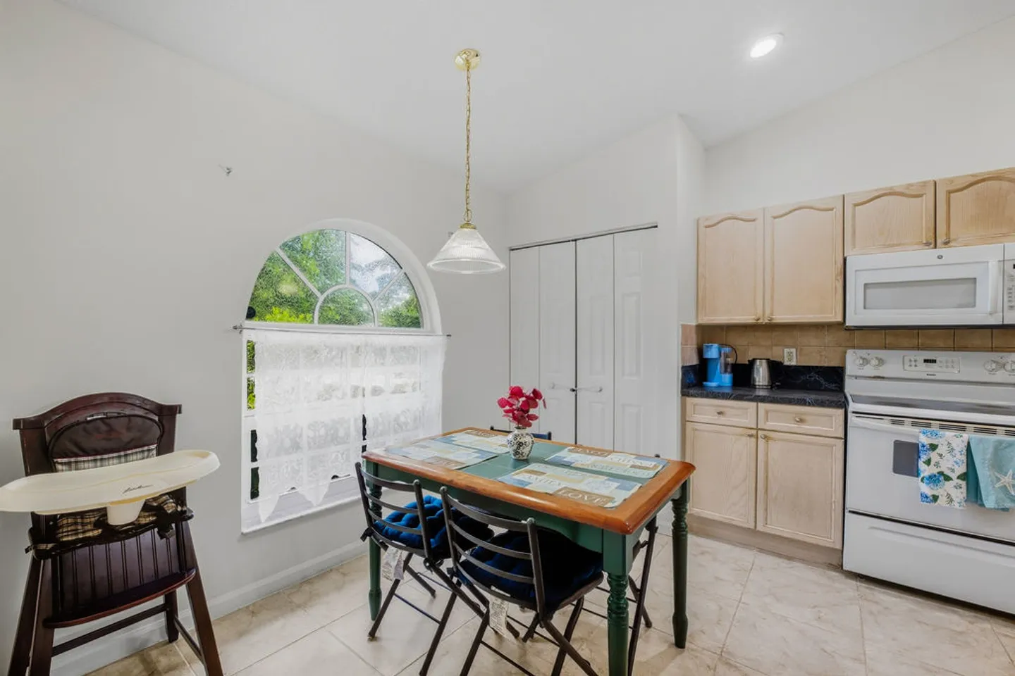 Kitchen dining nook with an arched window, a wooden table with chairs, a high chair, and light wood cabinetry.