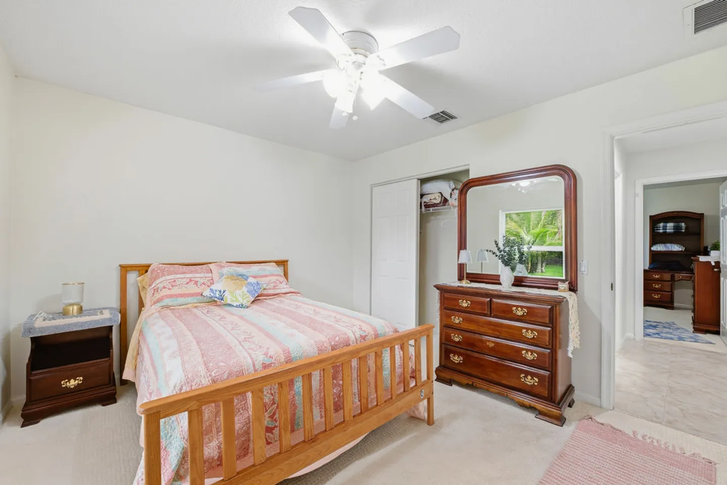 Bedroom featuring a wooden bed frame with a patterned quilt, matching wood nightstand, dresser with mirror, and a ceiling fan.