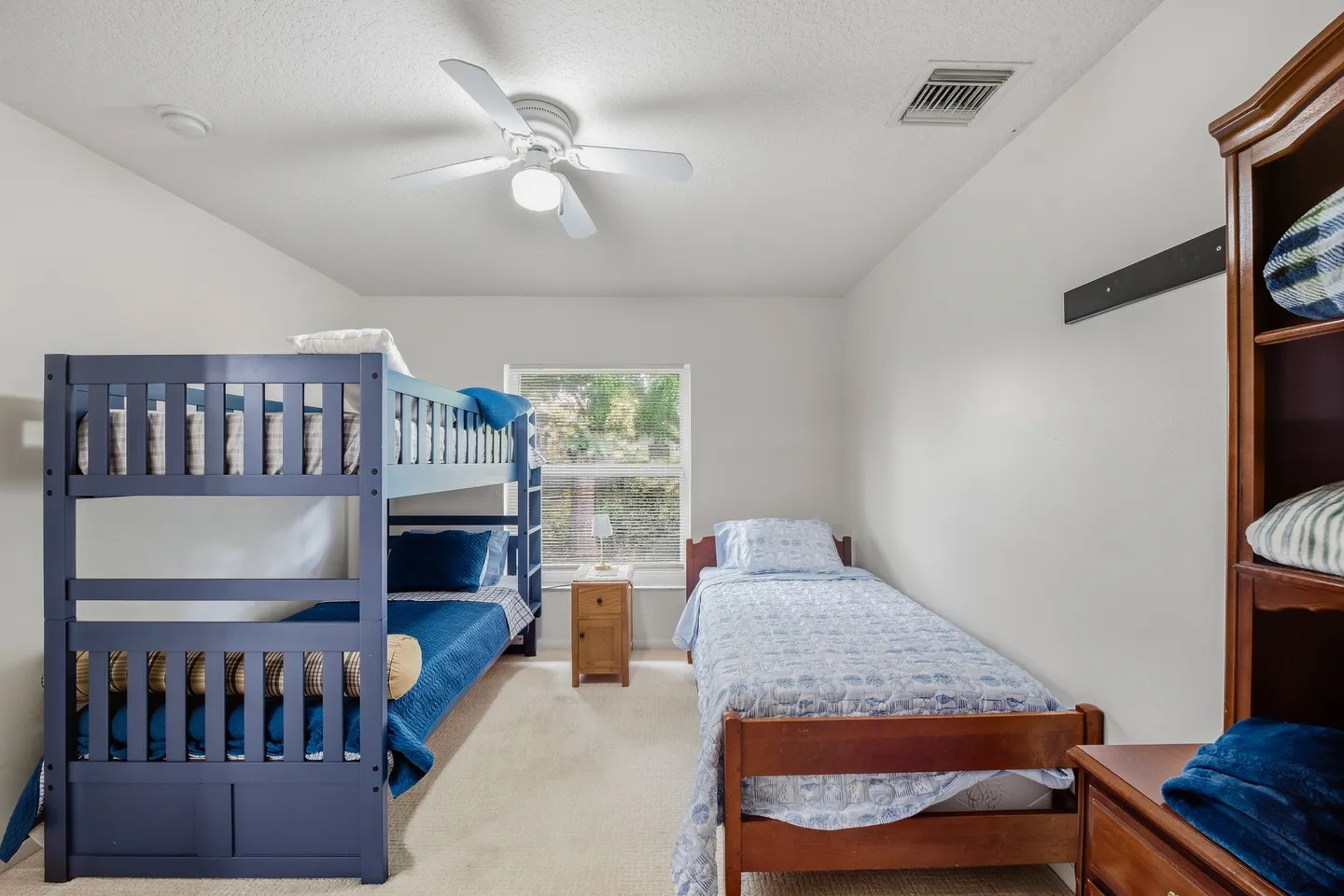 Bedroom featuring a blue wooden bunk bed on the left, a single wooden bed on the right, and a window in the center.