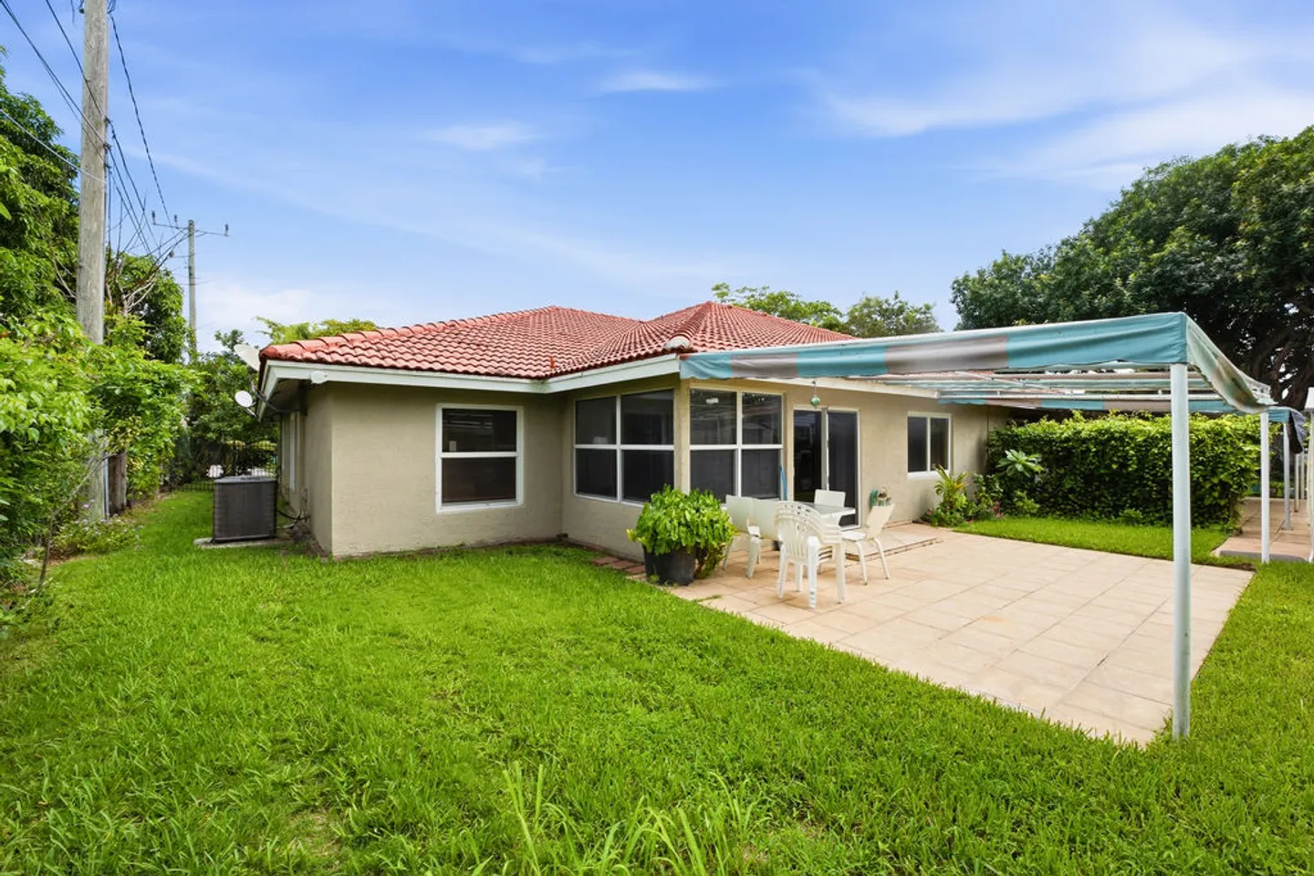 Rear exterior of a single-story home with a red-tiled roof, grassy yard, and tiled patio area with an awning and outdoor seating.