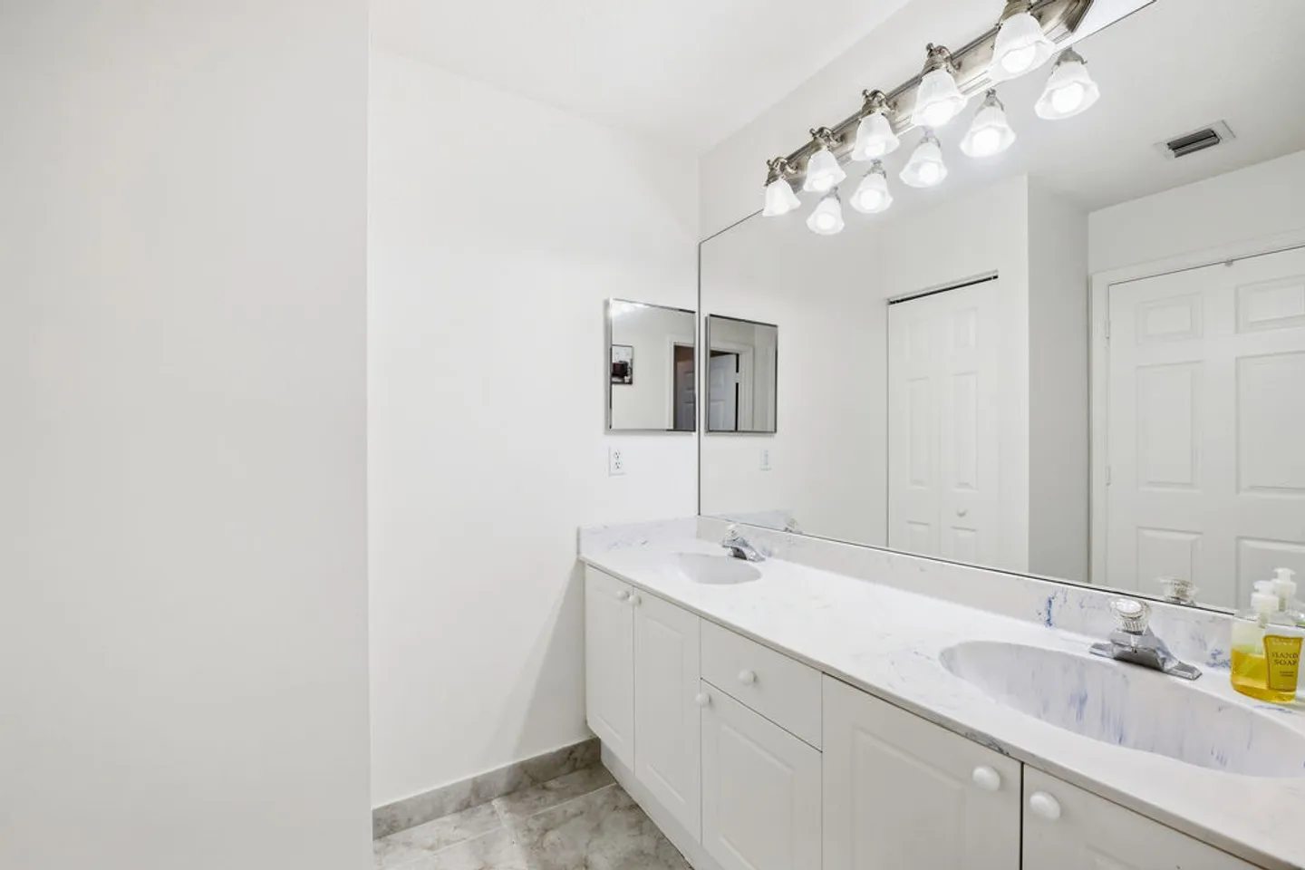 Bathroom featuring a double-sink vanity with white cabinets and a large mirror topped by vanity lights.