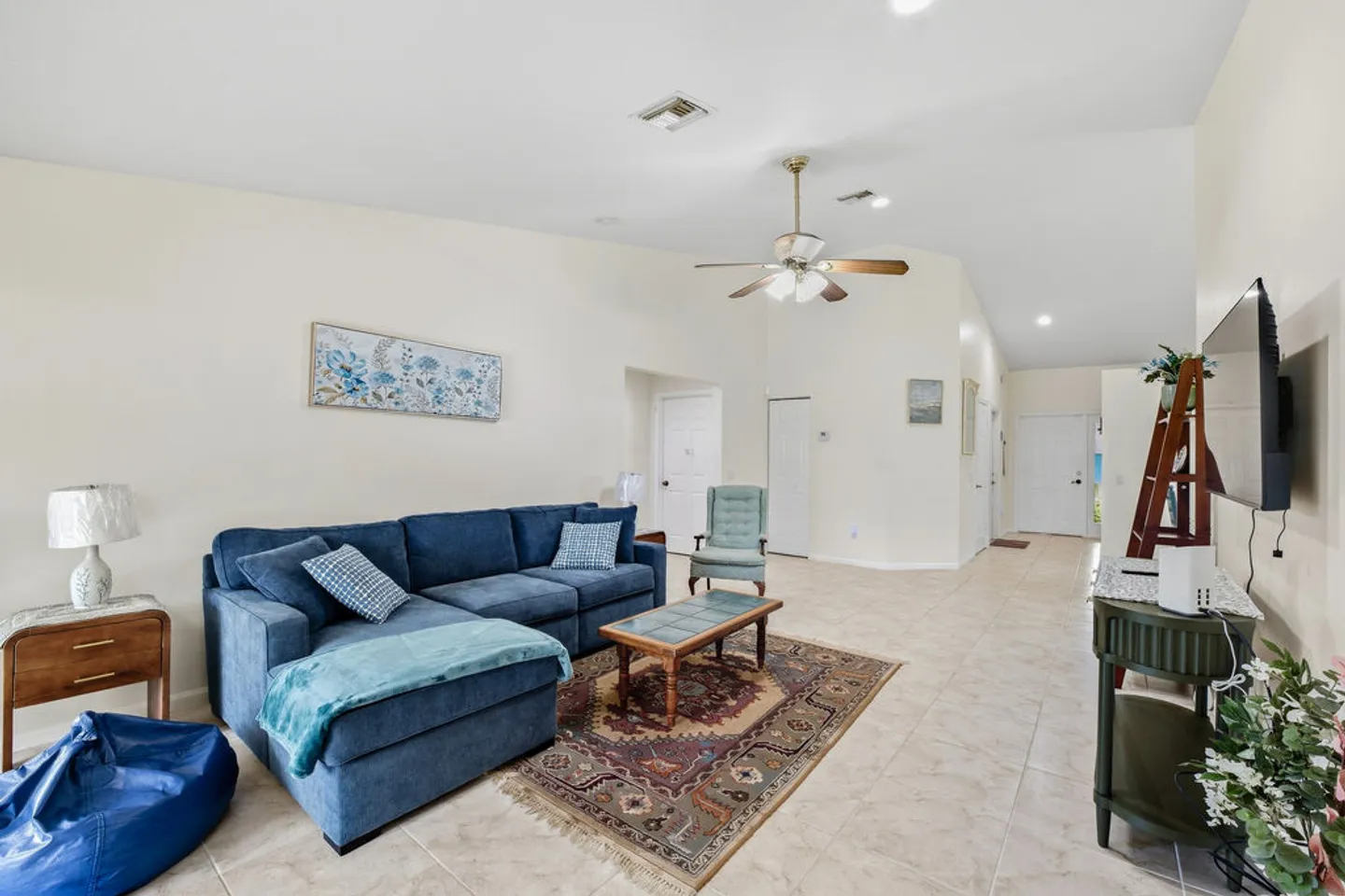 Living room featuring a blue sectional sofa, a coffee table on a patterned rug, tiled floors, and a ceiling fan.