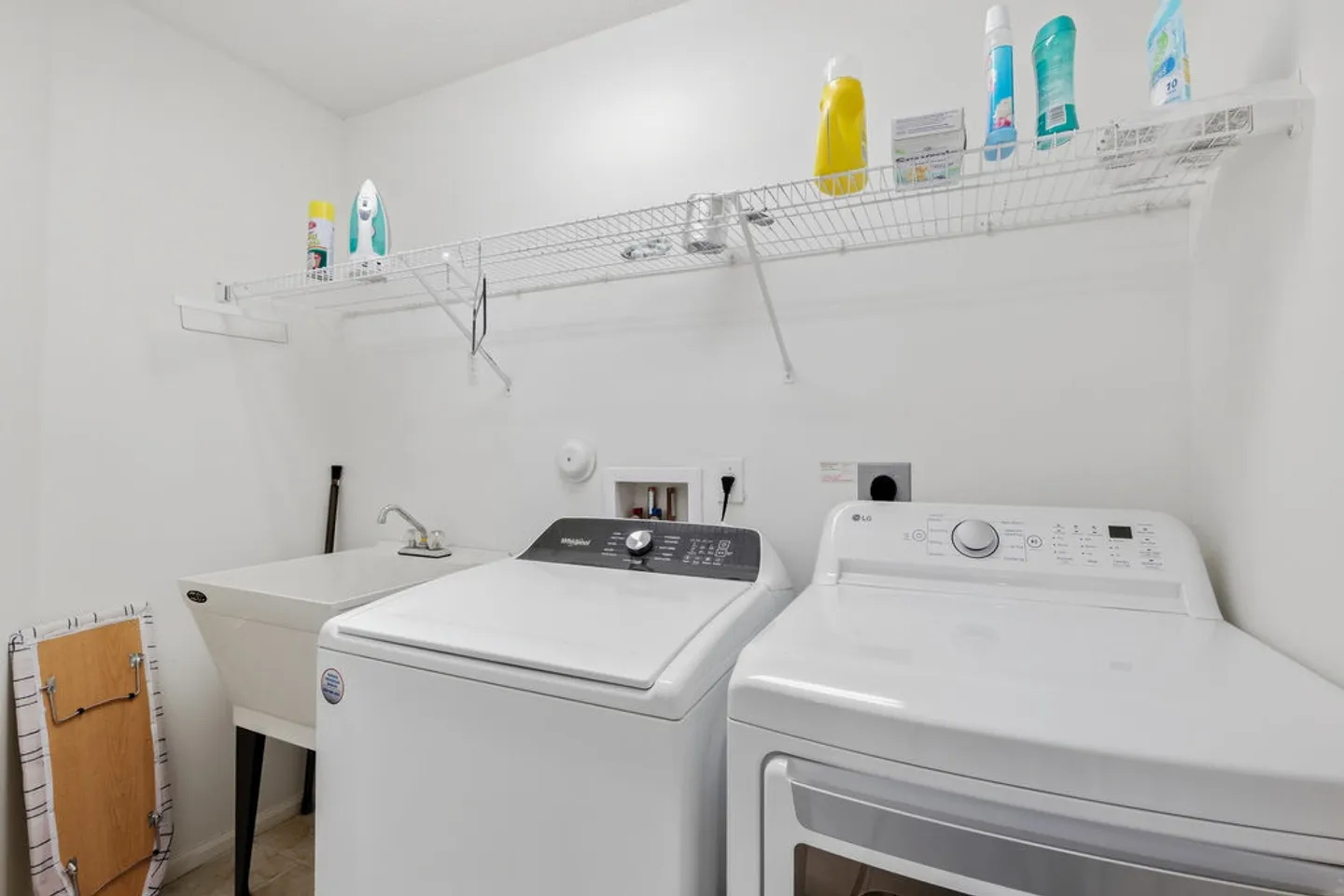 Laundry room with a top-load washer, front-load dryer, utility sink, and wall-mounted wire shelf.