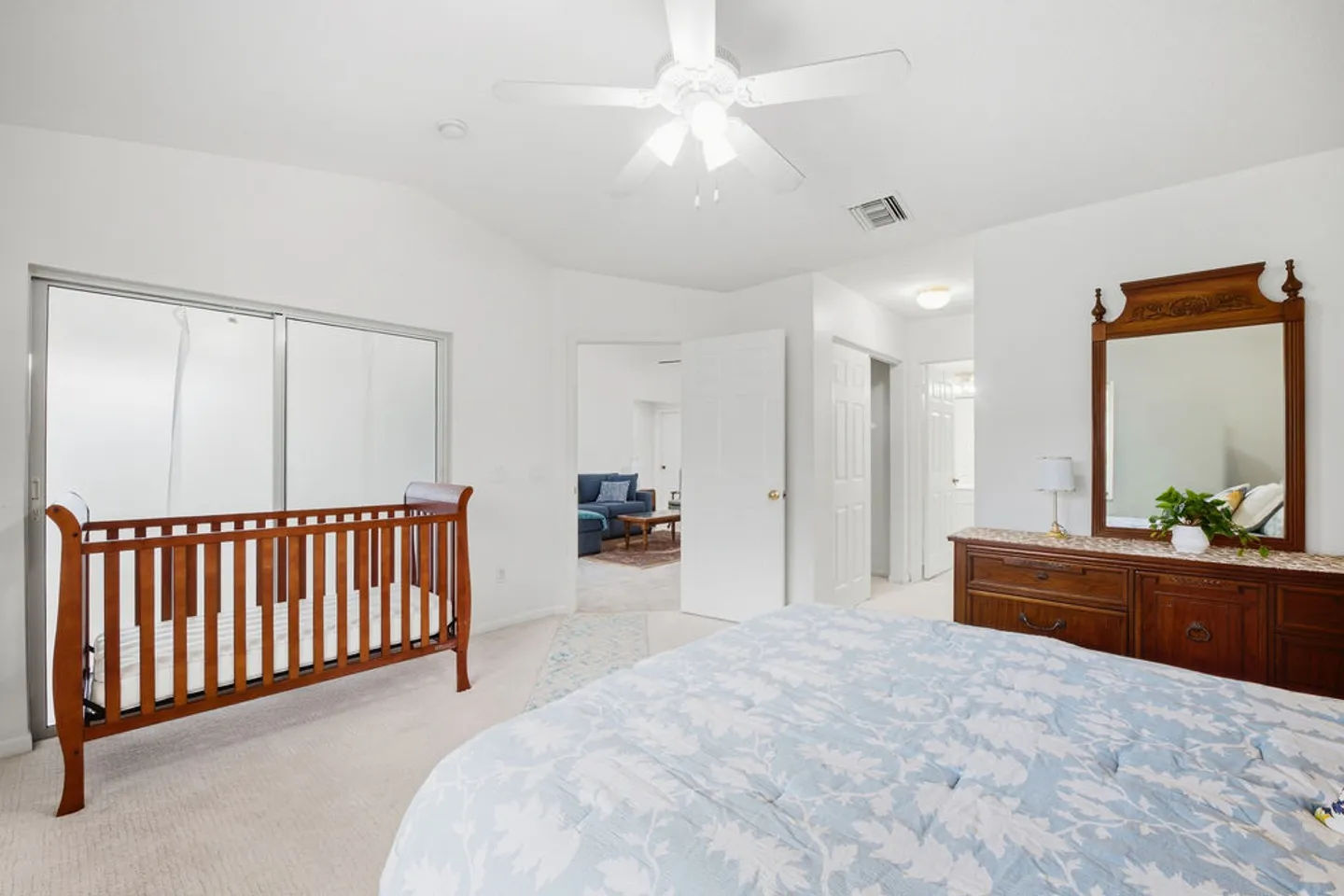 Bedroom featuring a wooden crib, large bed with a light blue floral bedspread, ceiling fan, and wooden dresser with a mirror.
