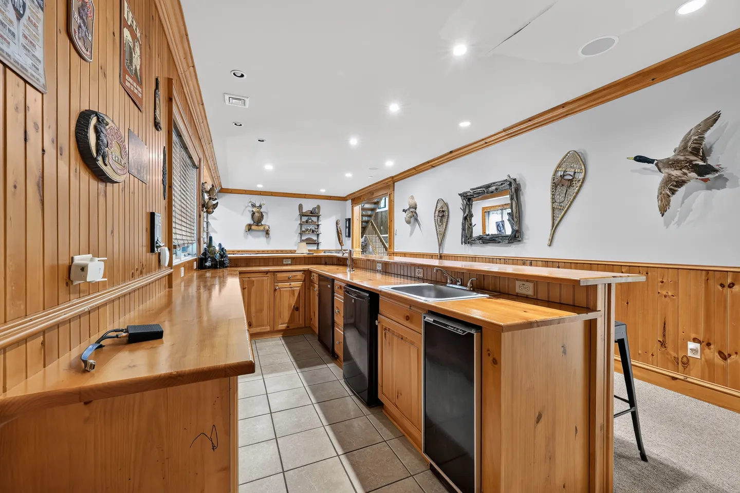 Wet bar area featuring pine cabinetry, under-counter appliances, a sink, and rustic decor on the walls.