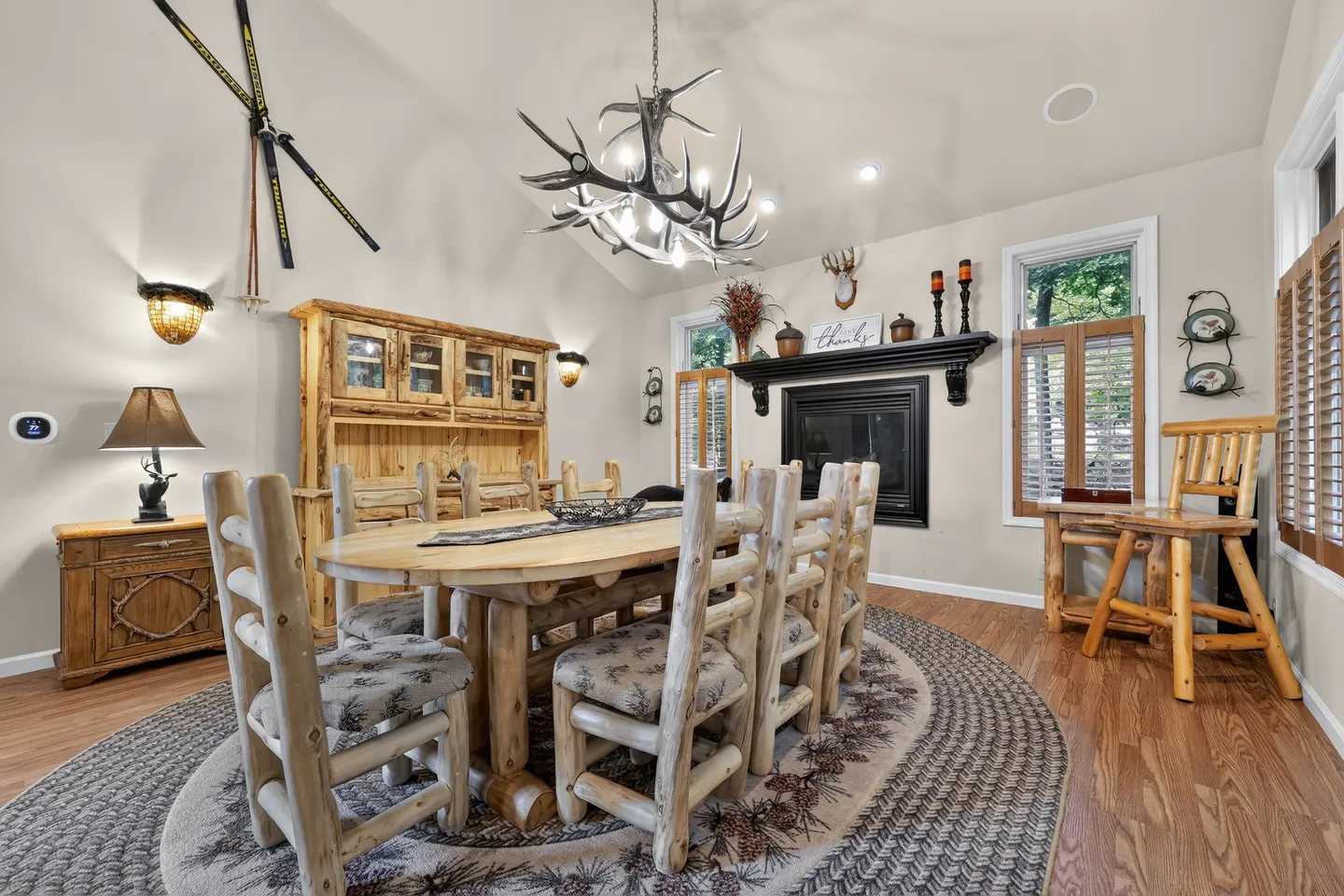 Dining room with a log dining table, matching chairs, an antler chandelier, and a fireplace with a dark mantel.