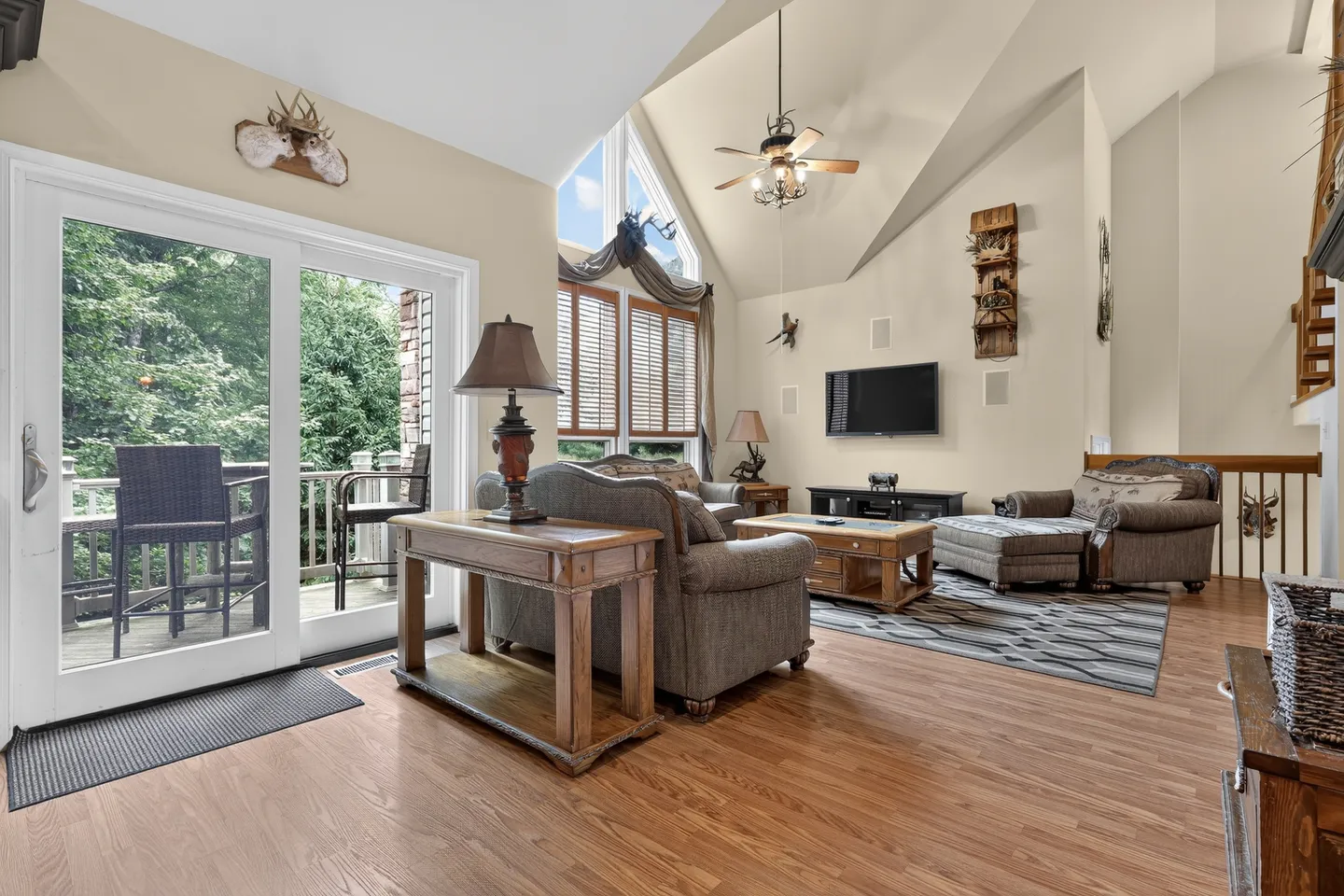 Living room with vaulted ceiling, wood-look flooring, upholstered seating, mounted TV, and sliding glass doors opening to an outdoor deck.