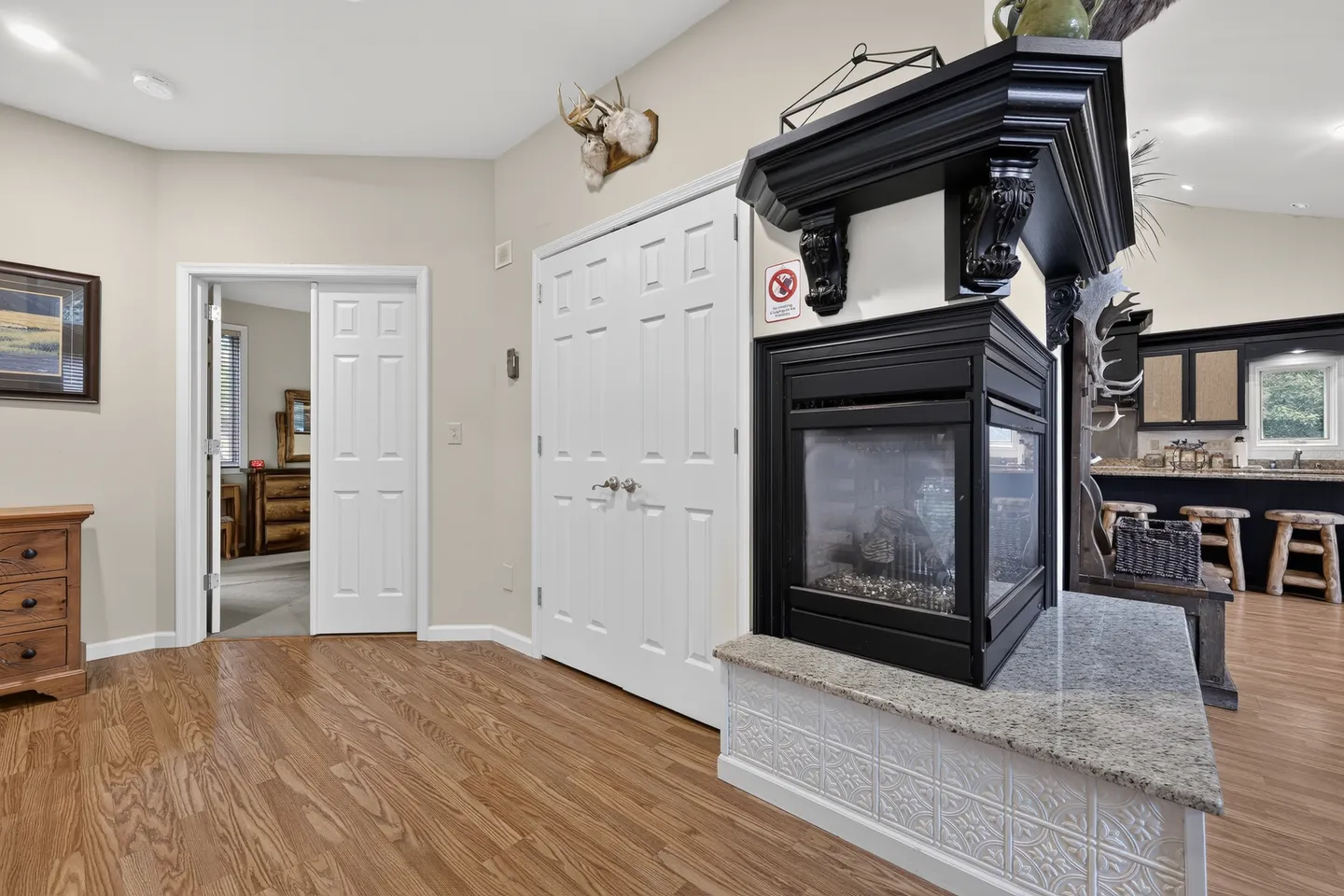 Living area hallway featuring wood flooring, white interior doors, and a corner multi-sided fireplace with a black mantle.