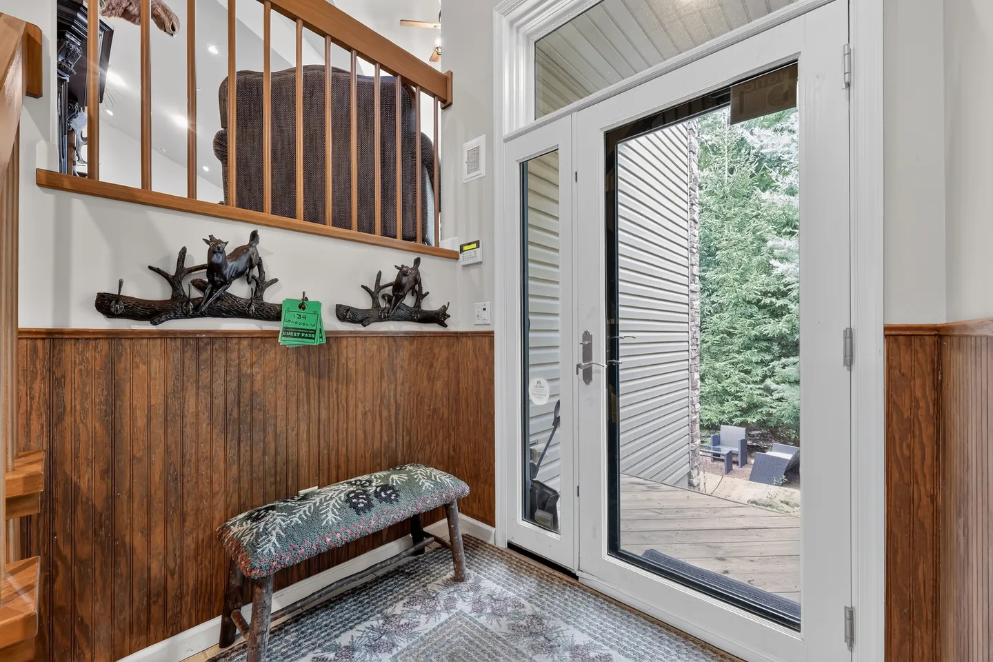 Entryway with a glass-paneled front door, side window, upholstered rustic bench, wood wainscoting, and a loft overlook.