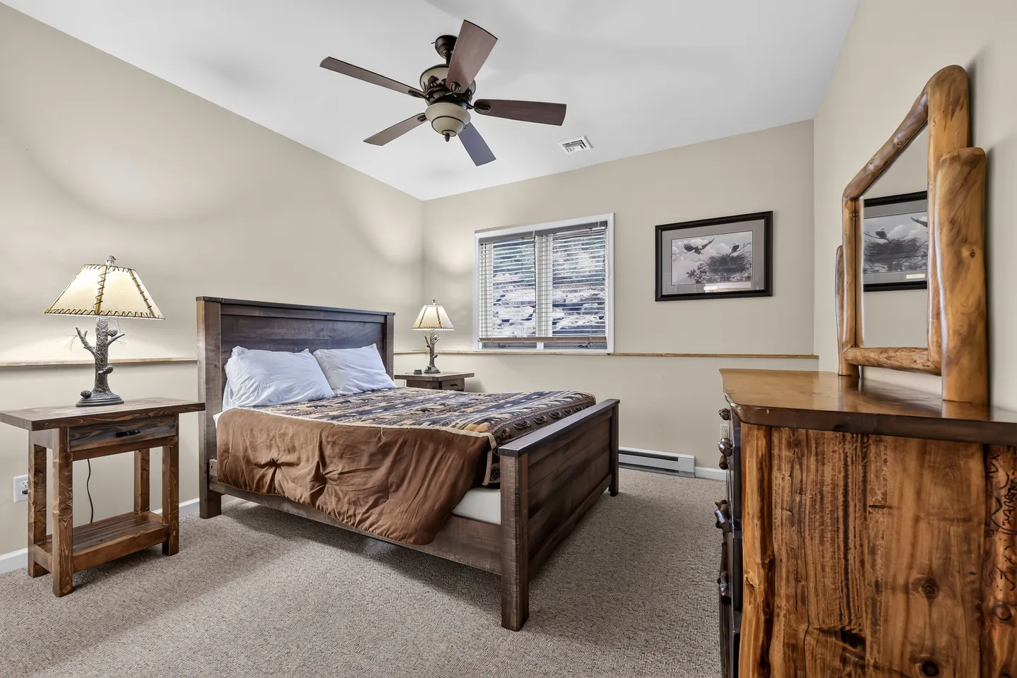 Bedroom with carpet, wood bed frame, rustic bedside tables with lamps, dresser with mirror, and ceiling fan.