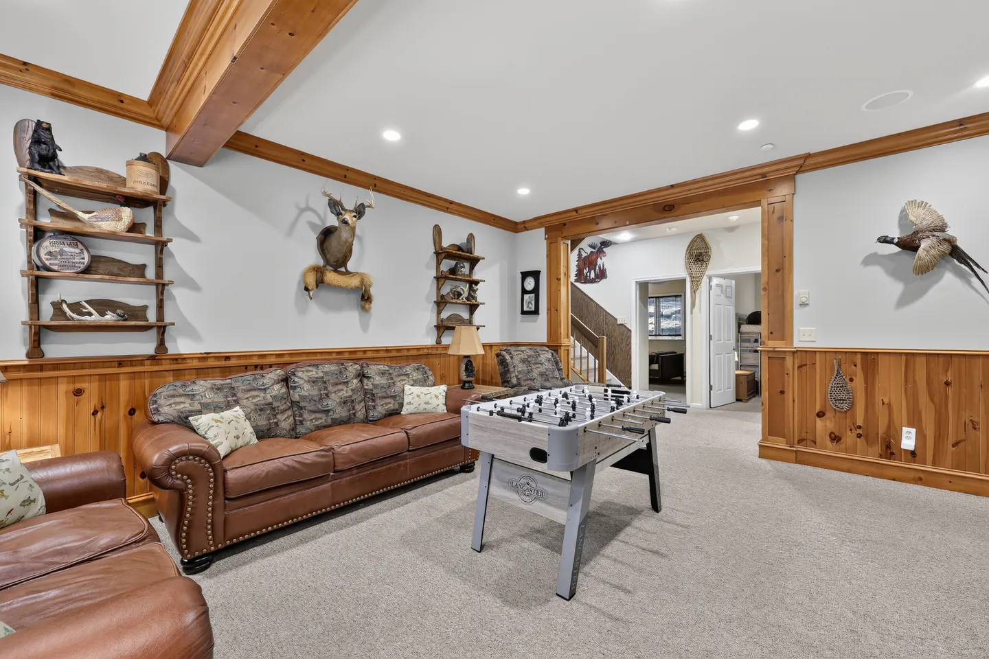 Game room featuring carpeted floors, wood wainscoting, leather seating, a foosball table, and taxidermy mounts on the walls.