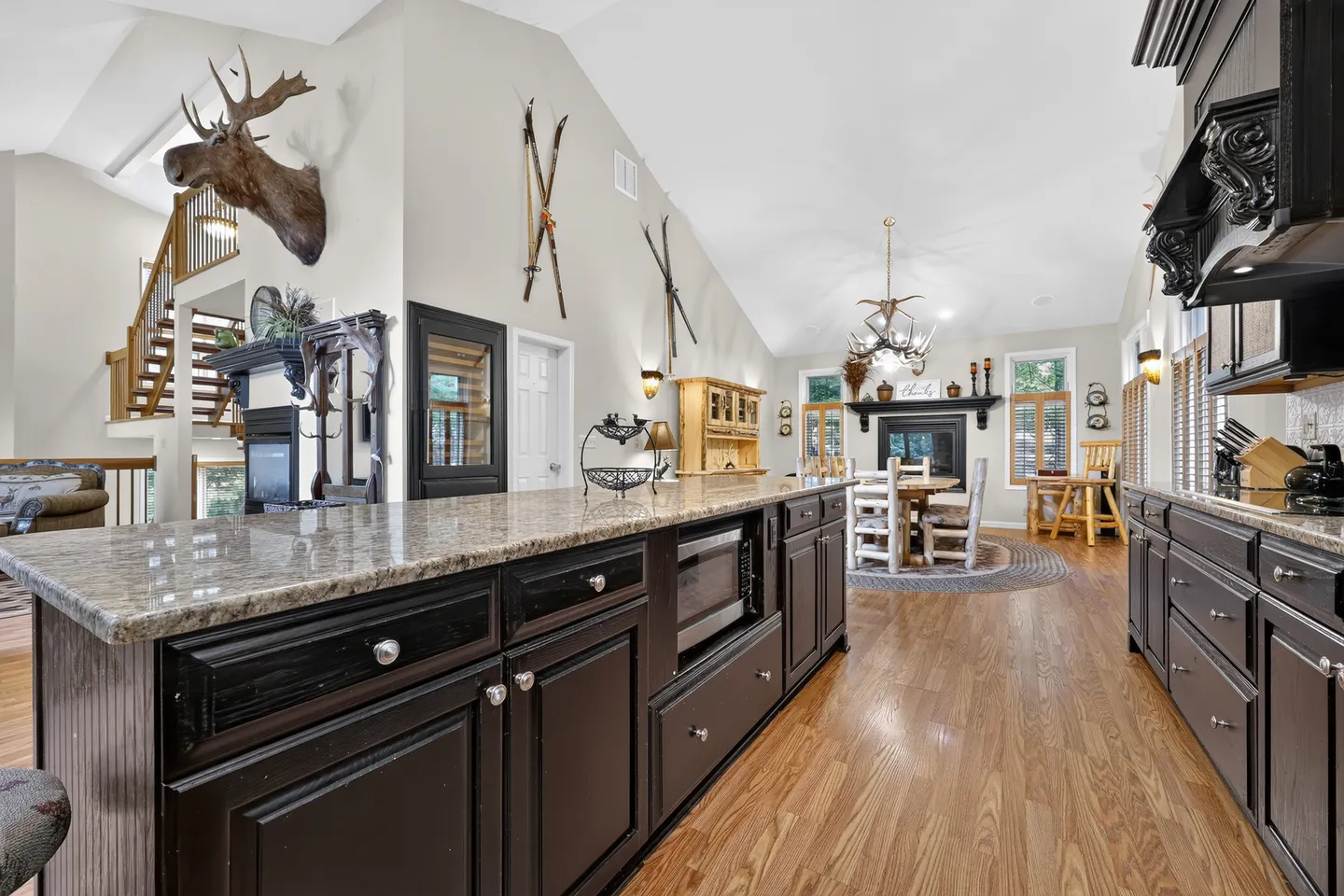 Open concept kitchen with a large dark island, vaulted ceilings, and a view into the dining area and staircase.