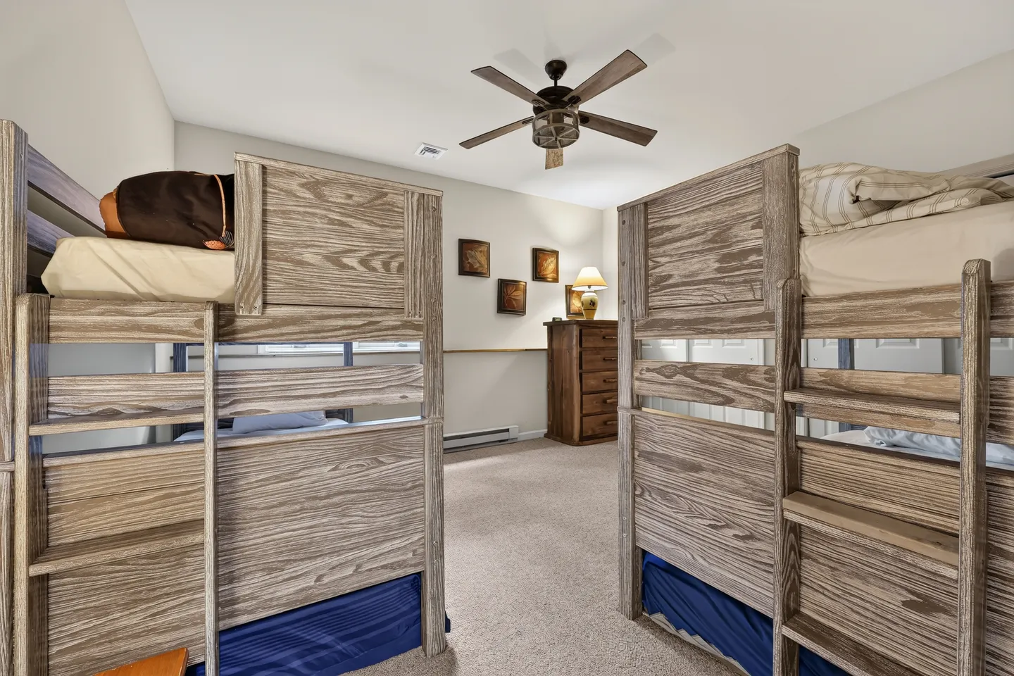 Bedroom with two sets of weathered wood bunk beds, carpeted floor, ceiling fan, and a wooden dresser.