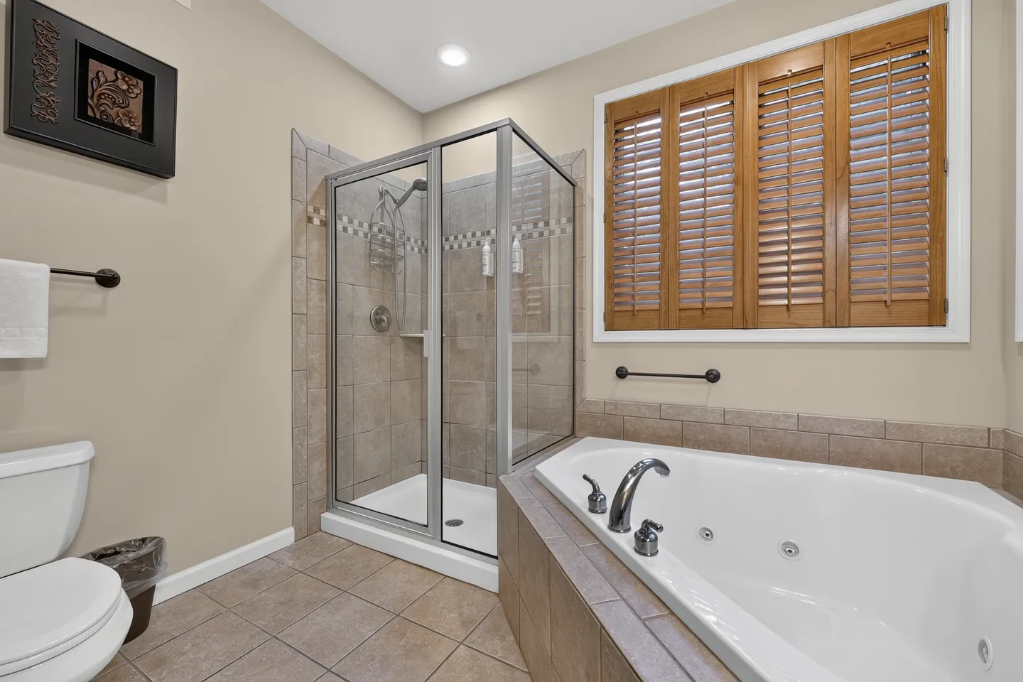 Bathroom with a tiled walk-in shower, corner jetted tub, toilet, and wooden window shutters.