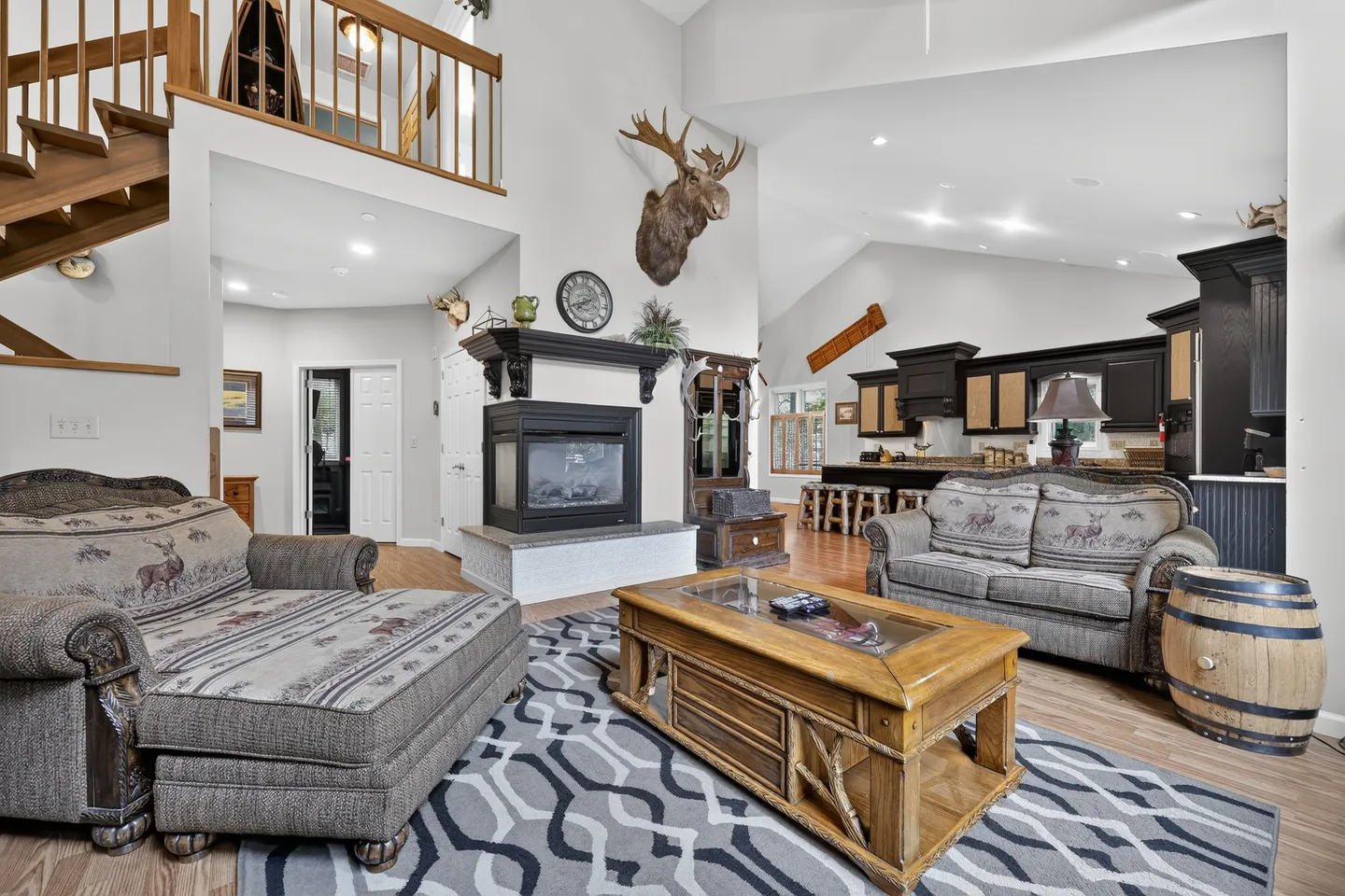 Open-concept living room with a fireplace, wildlife-themed upholstered seating, wood coffee table, and an open view to the kitchen and loft.