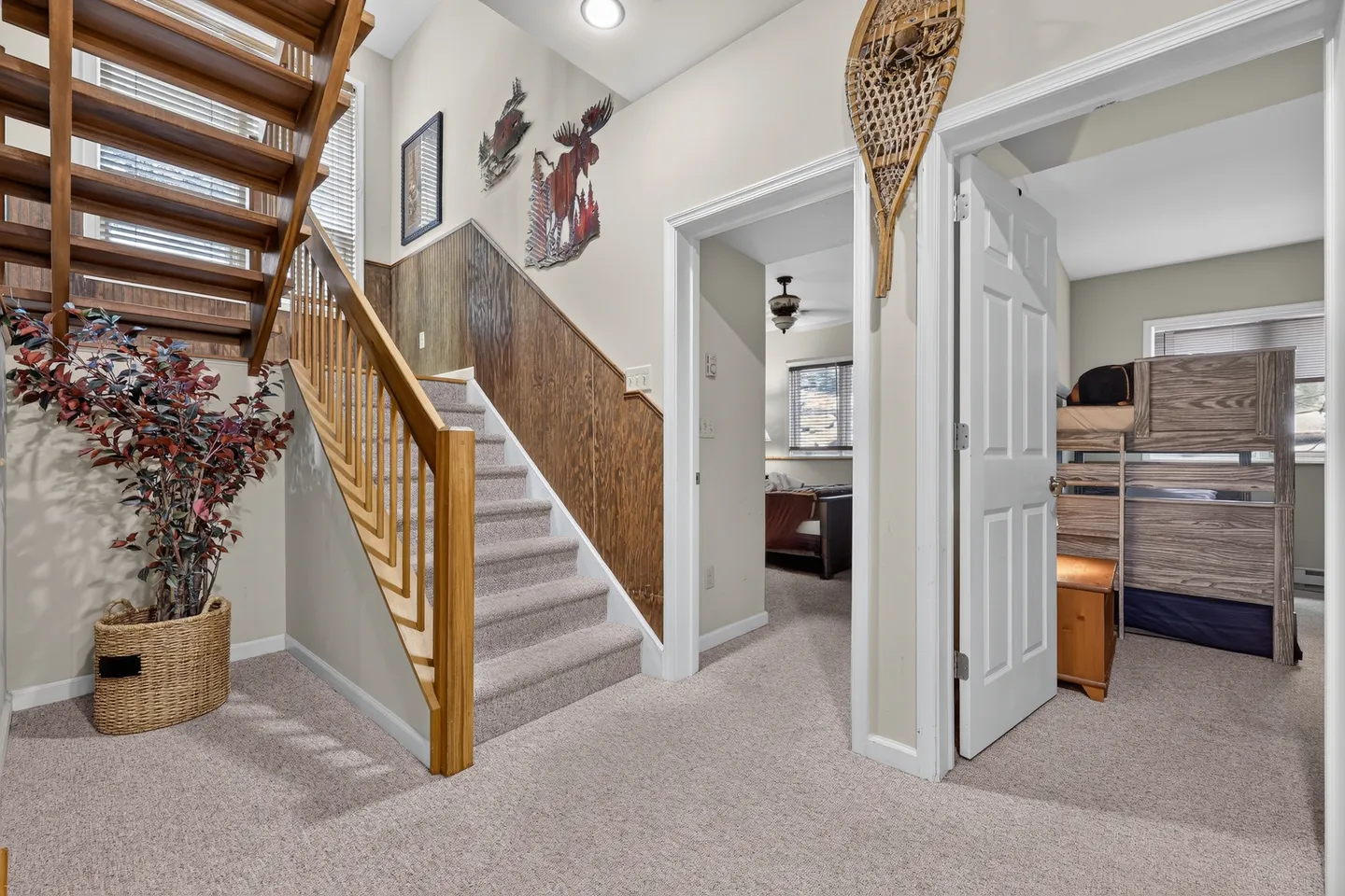 Hallway featuring carpeted floors, a wooden staircase, rustic wall decor, and doorways leading to adjacent rooms.