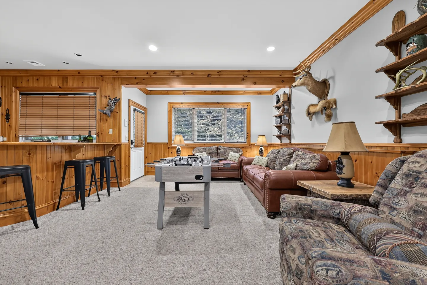 Game and living room featuring carpeted floors, wood wainscoting, leather sofas, a foosball table, and bar seating.