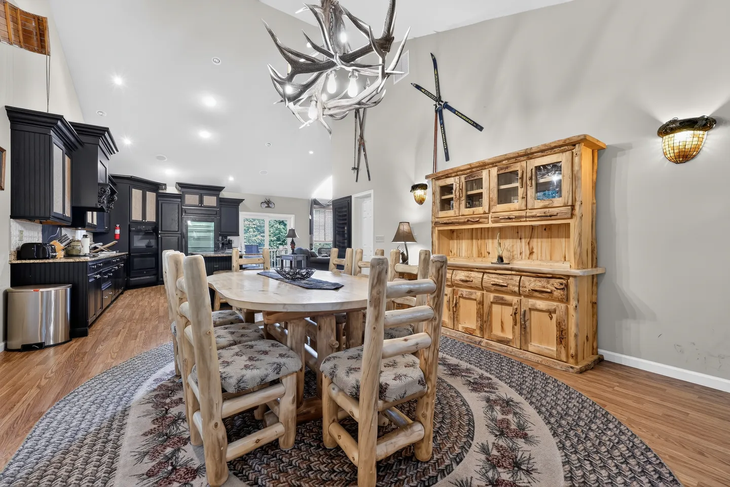 Dining area with a rustic log dining table, log chairs, antler chandelier, and a wood hutch next to an open kitchen.