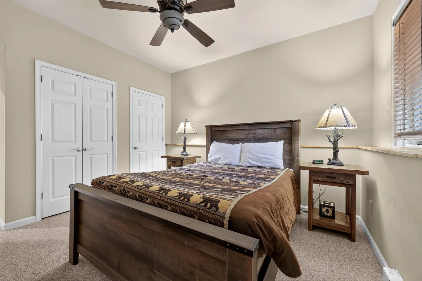 Bedroom with a wooden bed frame, patterned brown quilt, two nightstands with rustic lamps, and neutral walls.