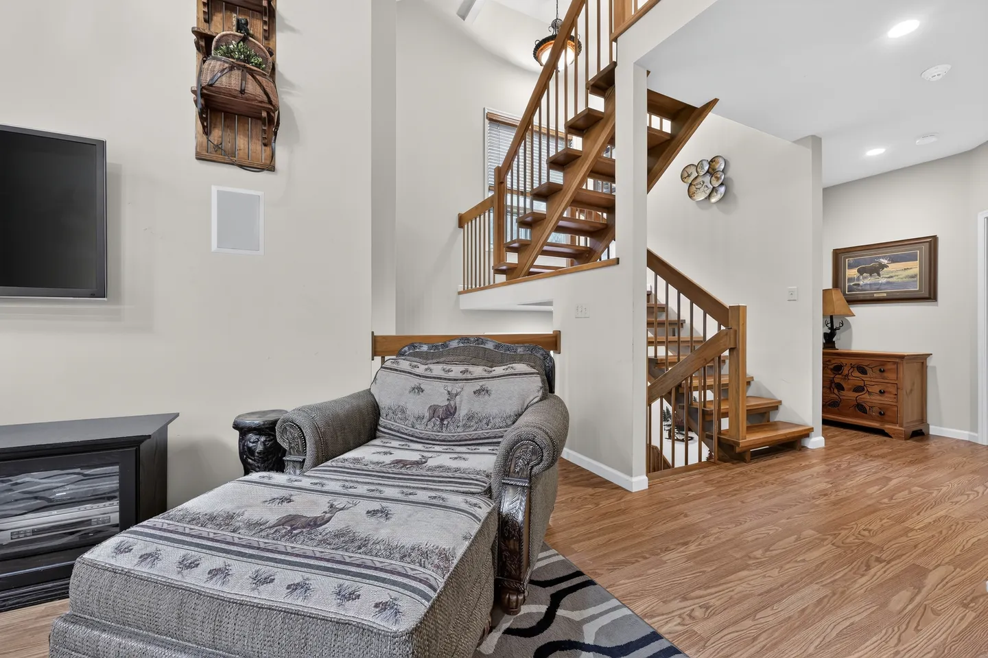 Living area featuring a patterned chaise lounge in front of an open wooden staircase leading to the upper level.