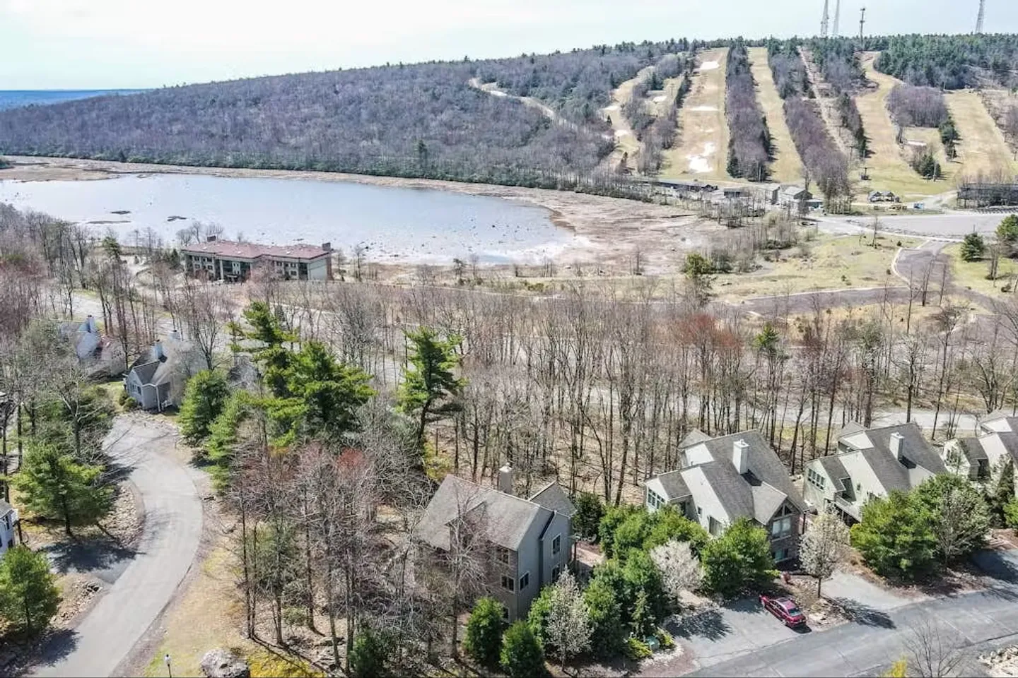 Aerial view of a neighborhood of townhomes nestled in trees near a lake and a ski mountain with ski slopes.