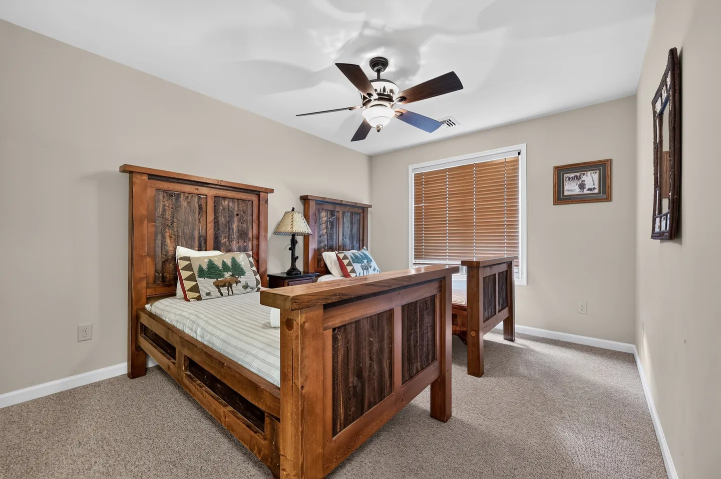 Bedroom with two rustic wooden beds, carpet flooring, a ceiling fan, and a window with wooden blinds.