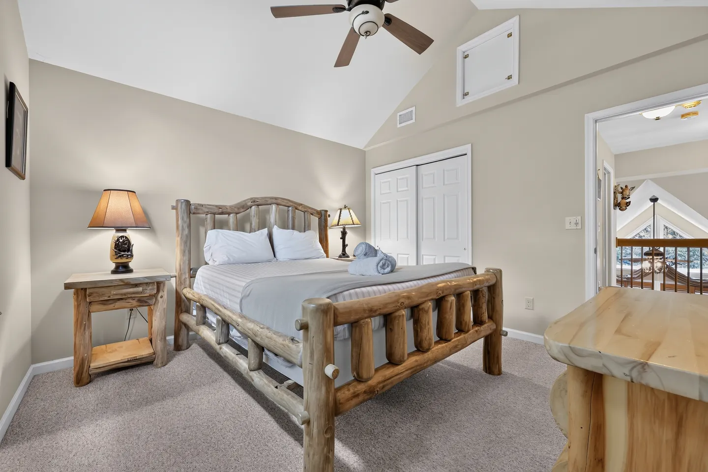Bedroom featuring a log-style bed frame, matching nightstand, vaulted ceiling, and carpeted floor.