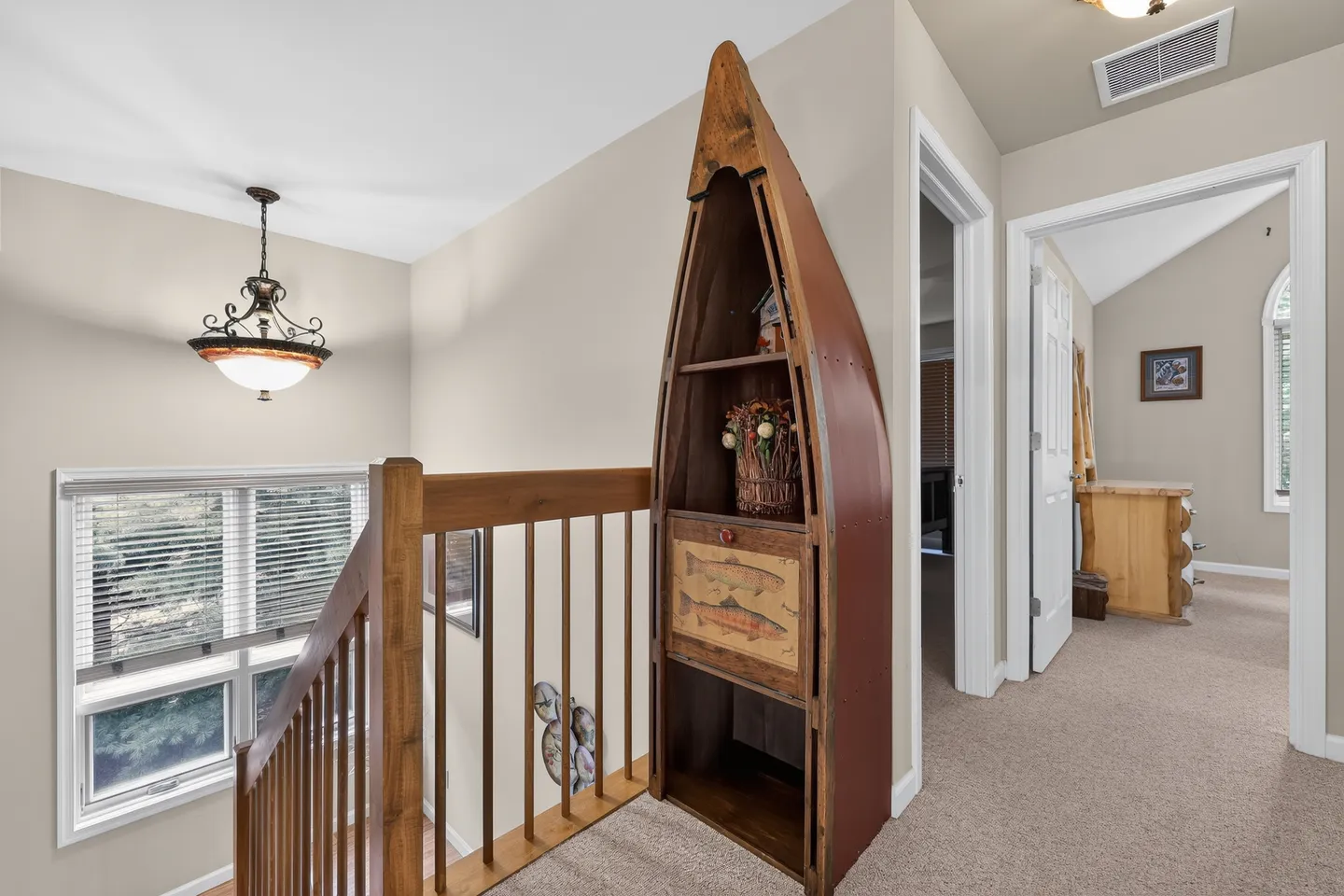 Upstairs landing with carpet, wood railing overlooking the stairs, and a canoe-shaped shelving unit.