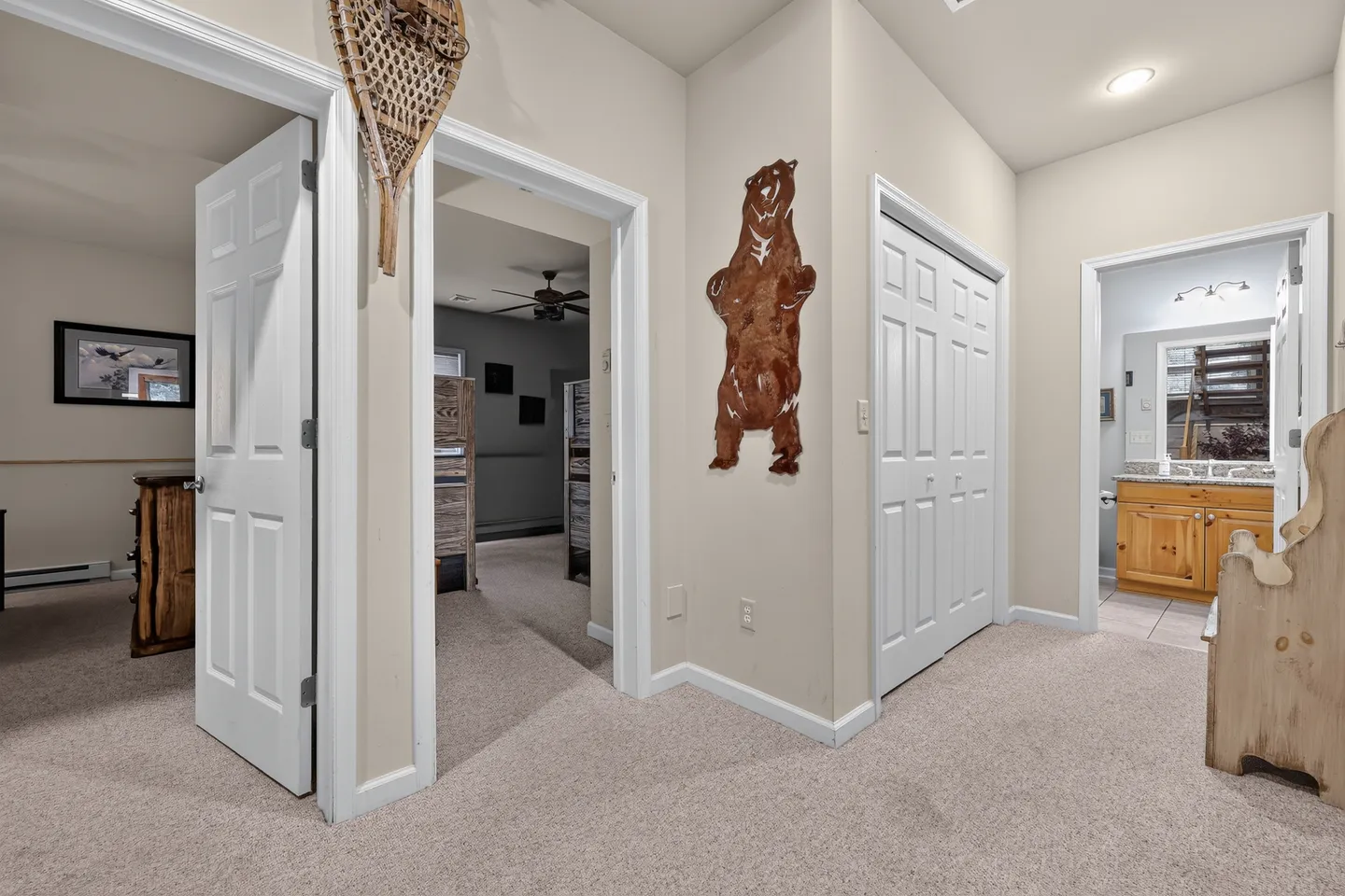 A carpeted hallway with open doors leading to bedrooms, a bathroom, and closet doors, featuring a bear wall cutout.