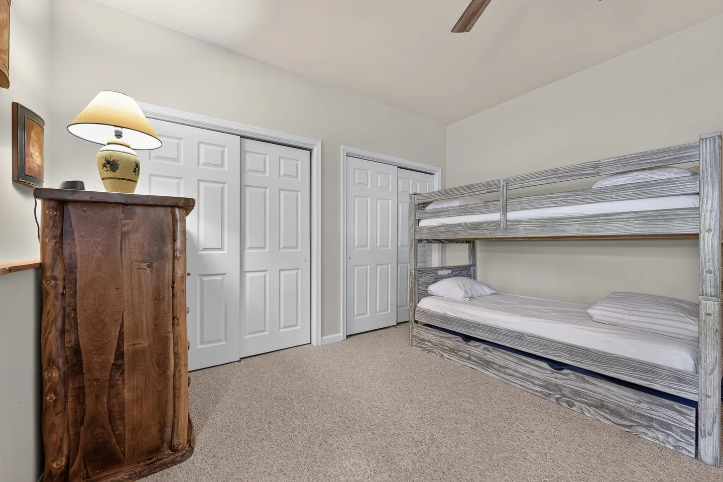 Bedroom with carpet, a rustic wood dresser with a lamp, two white closet doors, and a weathered wooden bunk bed.