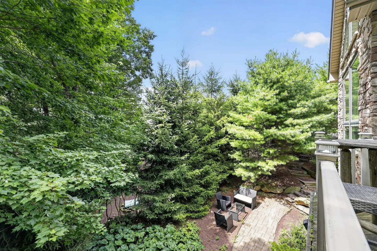 Elevated view from an upper deck overlooking an outdoor brick patio with seating surrounded by dense trees.