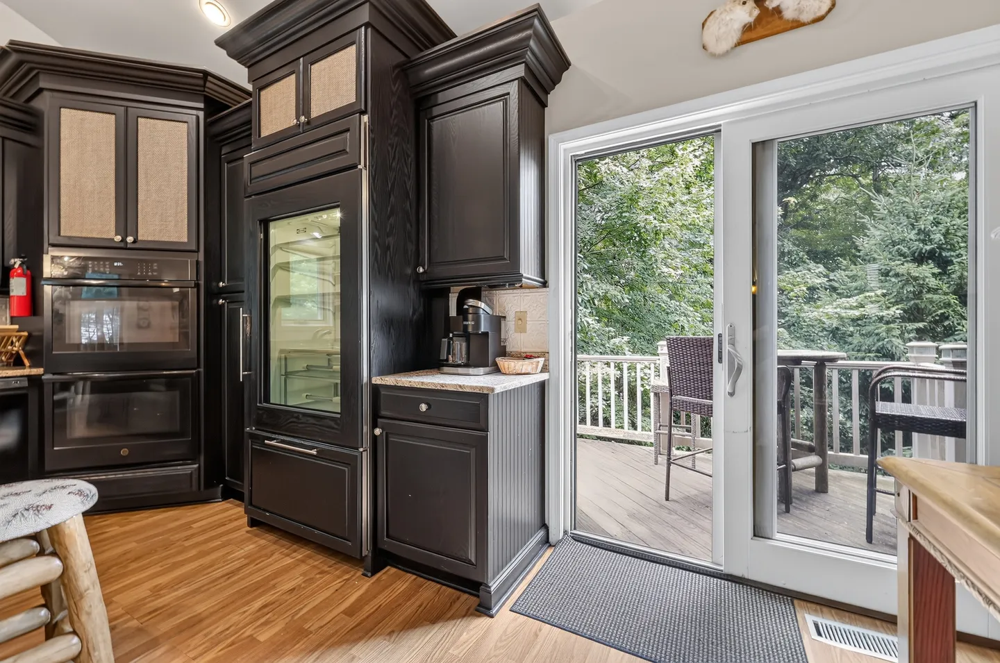 Kitchen interior featuring dark cabinetry, built-in ovens, a refrigerator with a glass door, and a sliding glass door leading to an outdoor deck.
