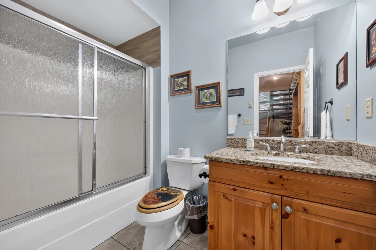 Bathroom with a wood vanity, granite countertop, toilet, and bathtub with sliding textured glass doors.
